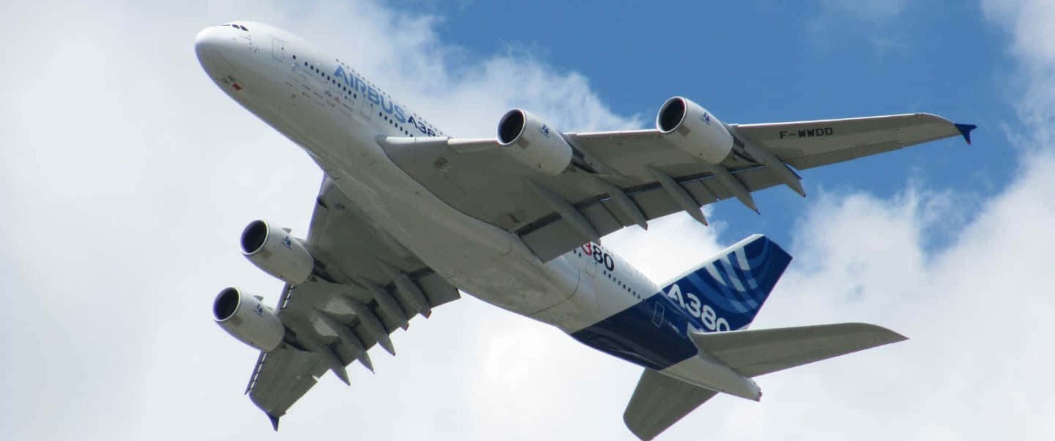 飛機 桌布 壁紙 — 一架巨大的空中巴士A380飛機在點綴著蓬鬆白雲的明亮藍天中翱翔。