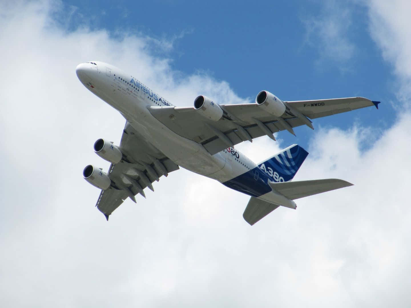 飛機 桌布 壁紙 — 一架巨大的空中巴士A380飛機在點綴著蓬鬆白雲的明亮藍天中翱翔。