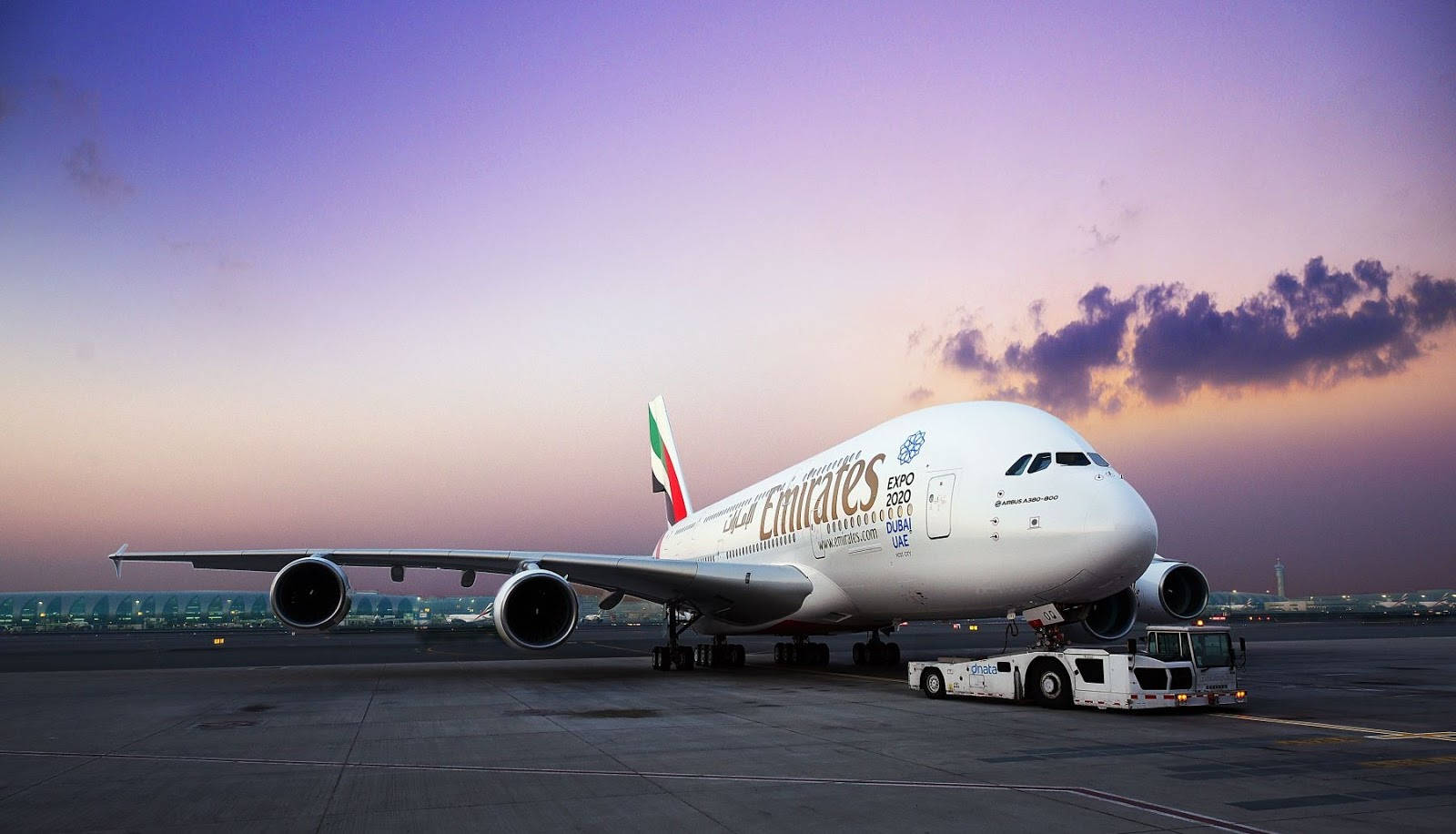雲朵 桌布 壁紙 — 一架巨大的阿聯酋航空空中巴士A380正在黃昏時分被拖過停機坪，上空是充滿活力的紫色和橙色天空。