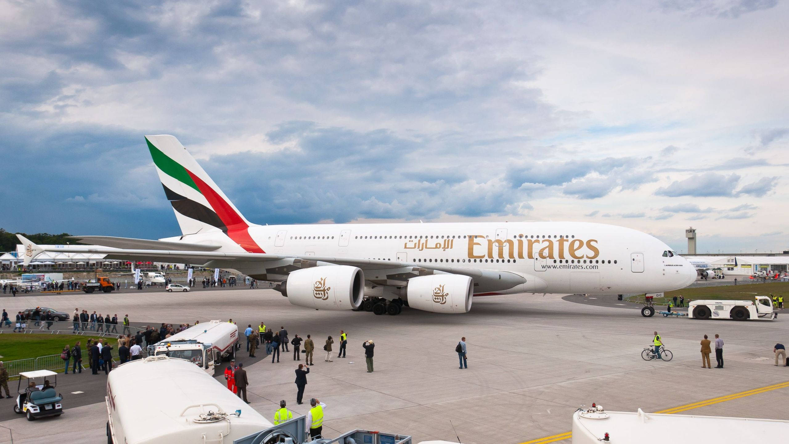 Plane 桌布 壁紙 — 一架巨大的阿聯酋航空空中巴士A380停放在機場停機坪上，天空多雲，附近有行人和地面車輛。