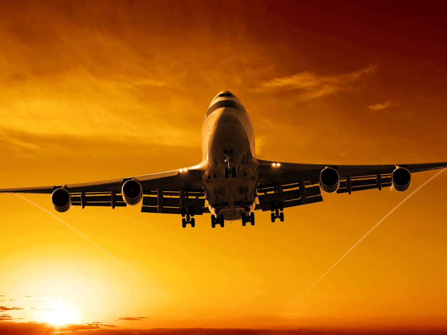 1440p Jumbo Jets 桌布 壁紙 — 一架巨大的飛機在火紅的橙色日落天空下下降，引擎發光，起落架已放下。