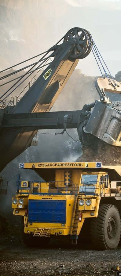 Dump Truck 桌布 壁紙 — 一架巨大的黃色礦用自卸車在明亮的日光下，於塵土飛揚的露天礦場中從巨型挖掘機接收煤炭。