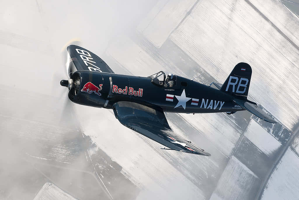 海盜船 桌布 壁紙 — 一架帶有 Red Bull 標誌的海軍藍色復古戰鬥機在雪地跑道上急轉彎，揚起白色粉末。