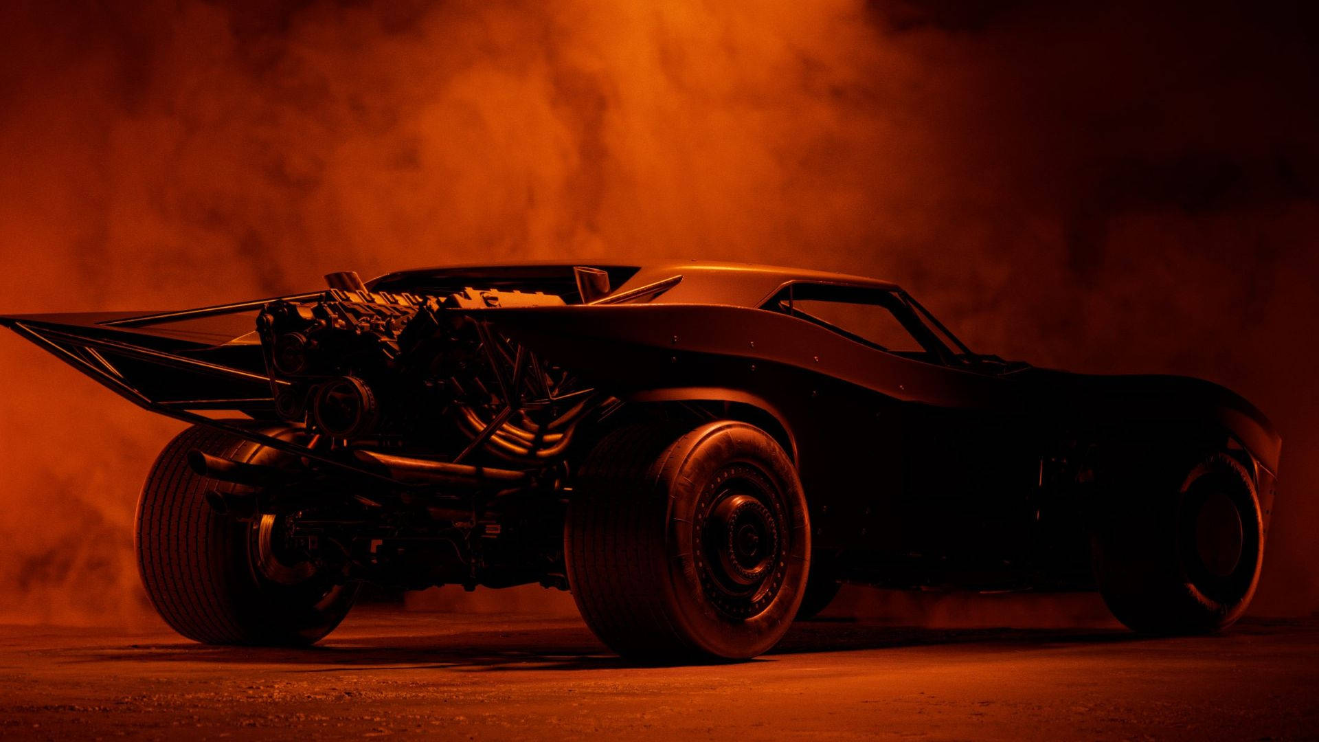 Batmobile 桌布 壁紙 — 一架帶有外露引擎和寬輪胎的威嚇黑色蝙蝠車，在戲劇性的低角度鏡頭下，於火橙色煙霧中發光。