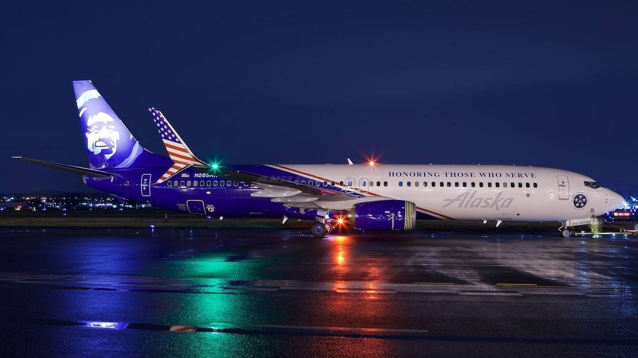 飛機 桌布 壁紙 — 一架帶有愛國塗裝的阿拉斯加航空飛機在夜間停在潮濕的停機坪上，反射出色彩繽紛的跑道燈光。