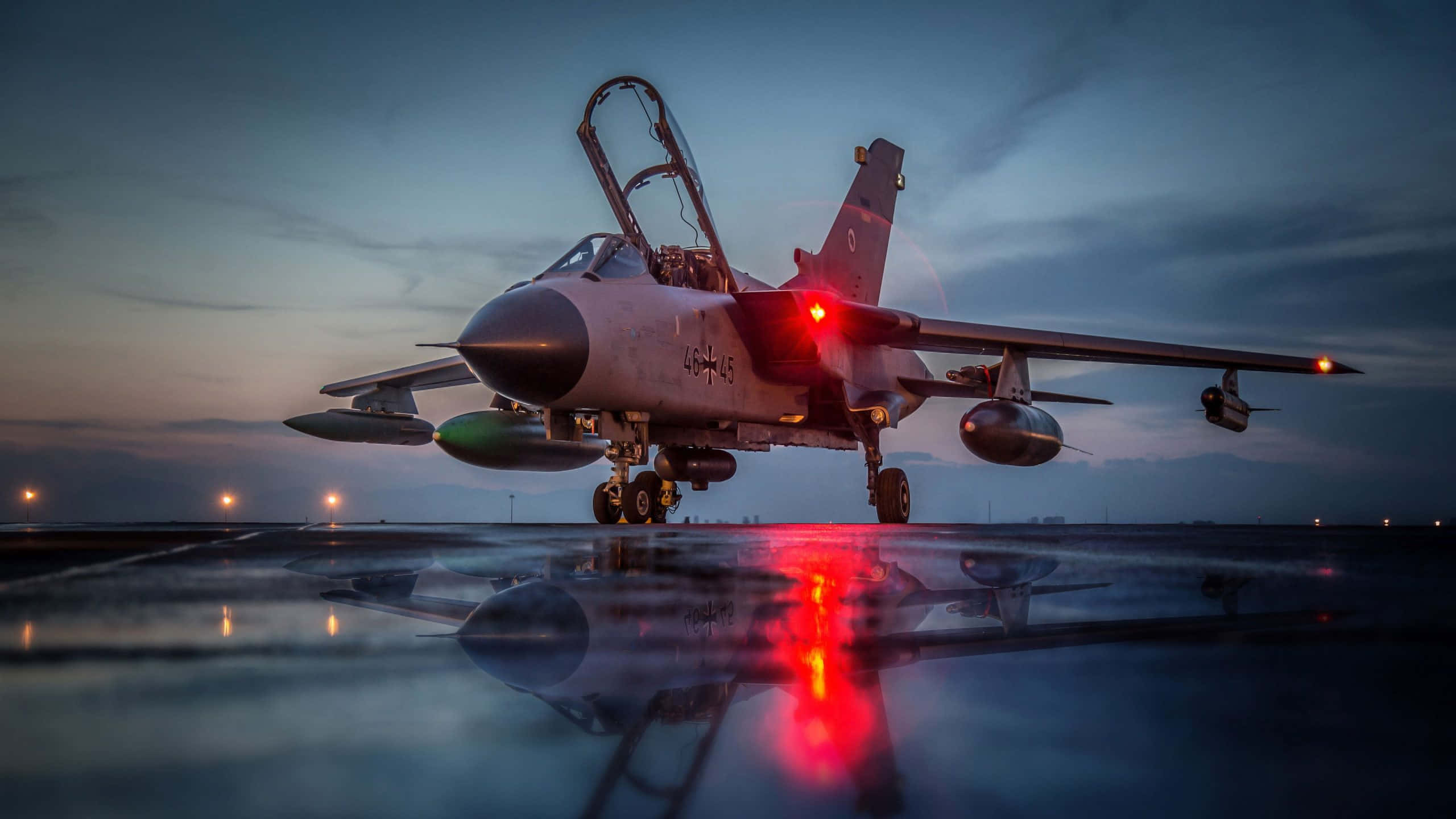 Aircraft 桌布 壁紙 — 一架帶有發光紅燈的戰鬥機在黃昏時分停在濕滑的跑道上，倒映在水坑中，天空陰沉。