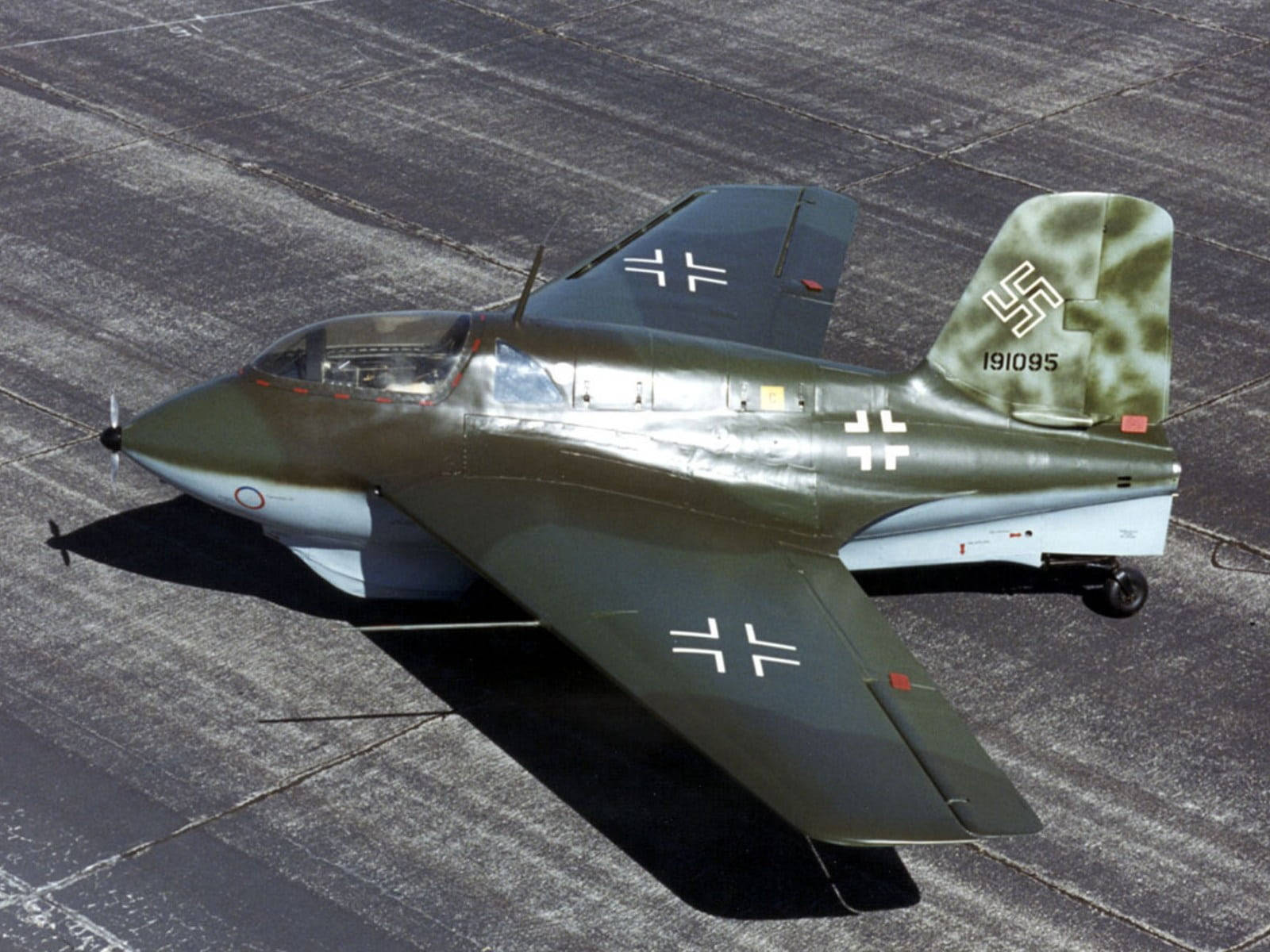 Aircraft 桌布 壁紙 — 一架帶有白色十字和卐字標記的復古橄欖綠軍用噴射機，在明亮的陽光下停放在裂開的停機坪上。