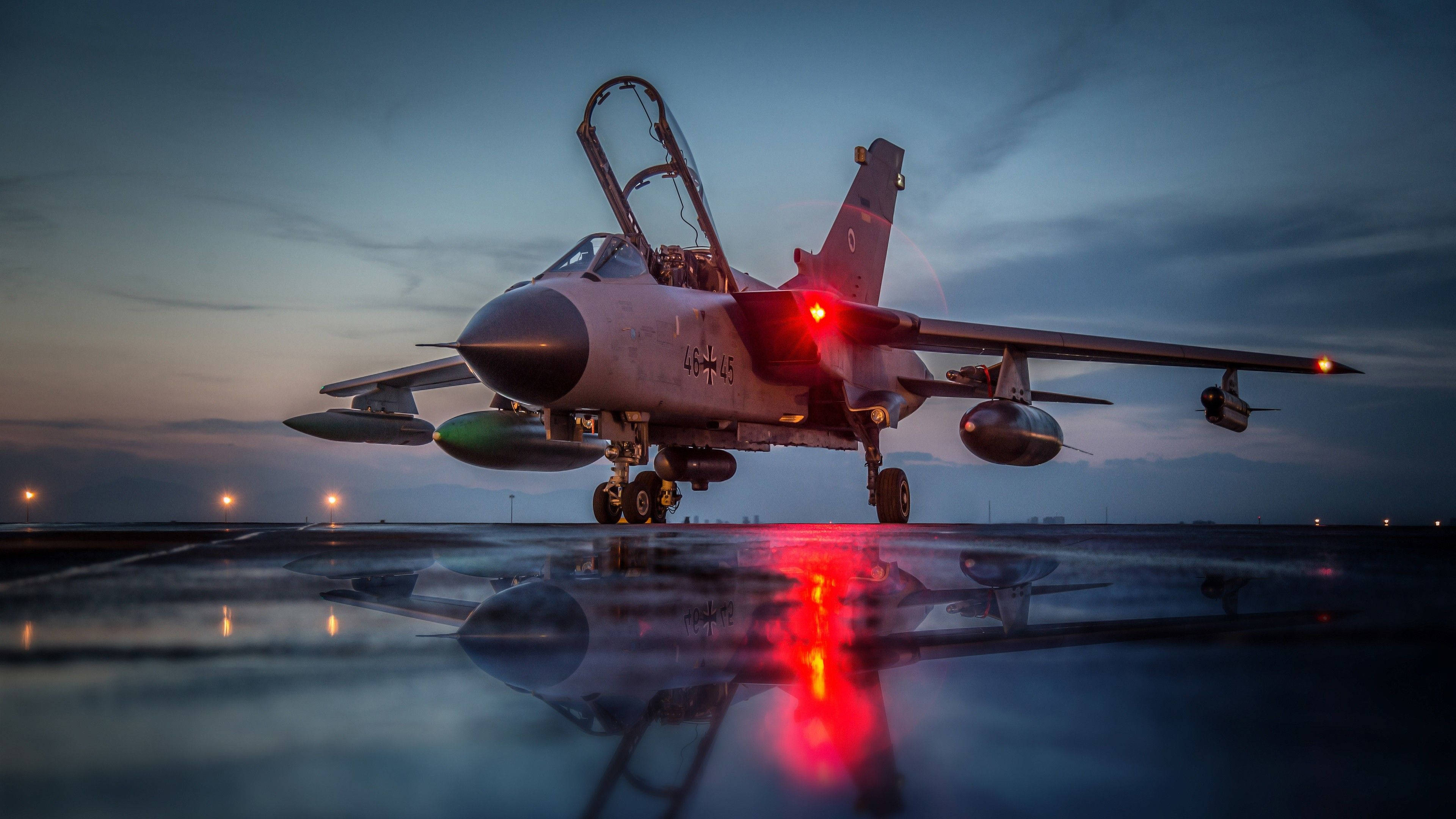 Air Force 桌布 壁紙 — 一架帶有紅色導航燈的戰鬥機在黃昏時停在潮濕的跑道上，在陰天下的水坑中反射。