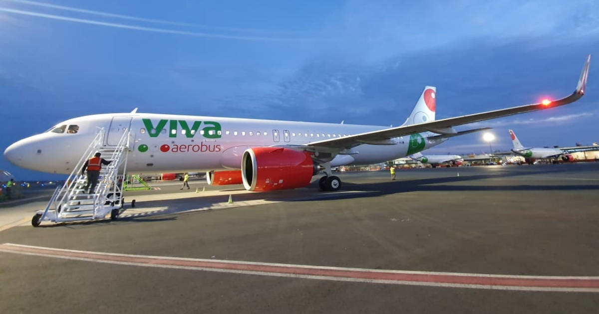 飛機 桌布 壁紙 — 一架帶有紅色引擎和綠色品牌的Viva Aerobus飛機，在黃昏時停在機場停機坪上，附近有地勤人員。