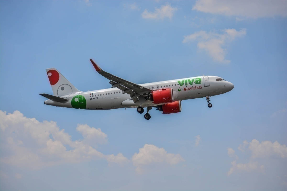 飛機 桌布 壁紙 — 一架帶有紅色引擎和綠色標誌的Viva Aerobus飛機在明亮的藍天和蓬鬆的白雲下低飛。
