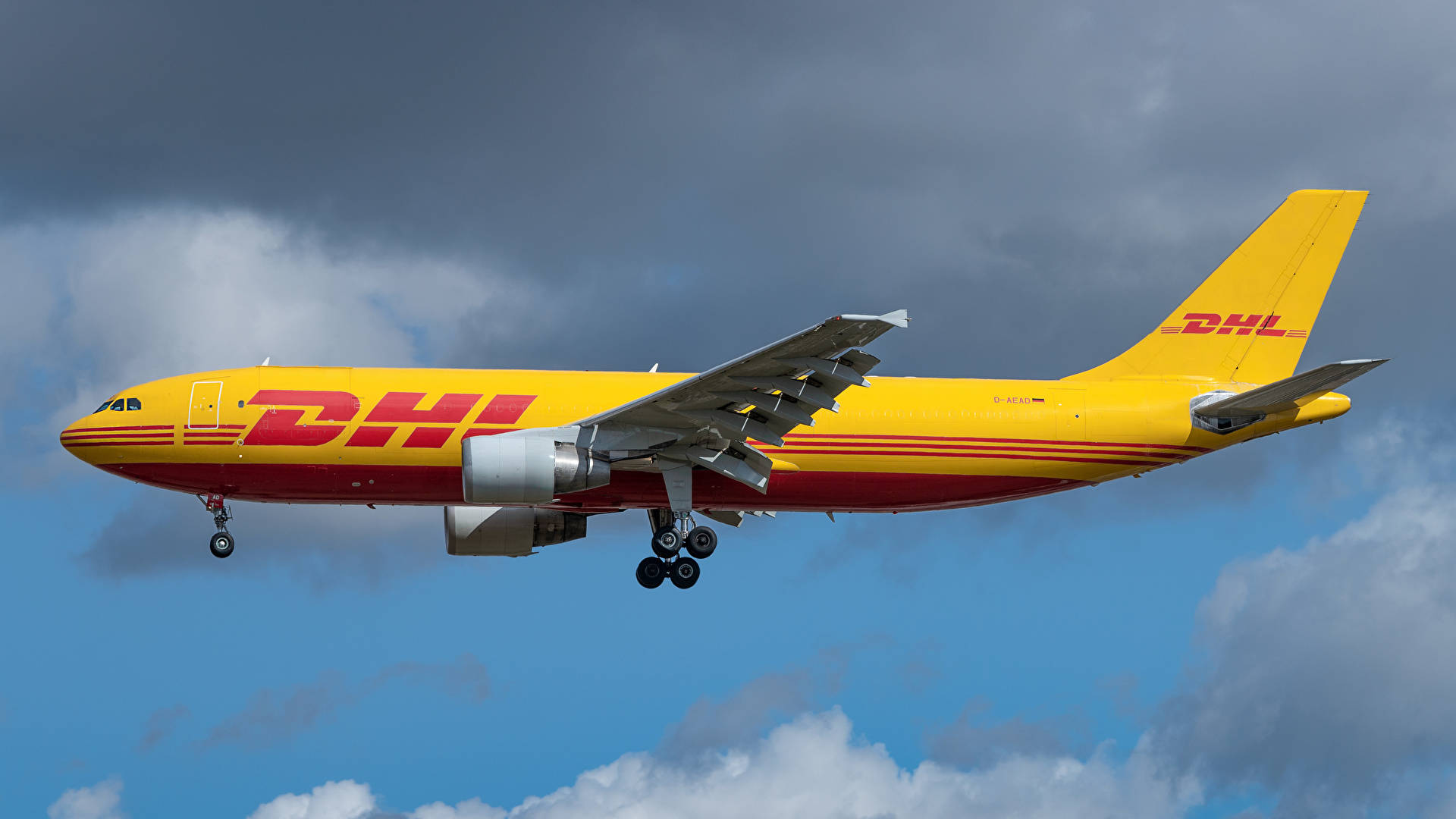 Dhl 桌布 壁紙 — 一架帶有紅色點綴的亮黃色DHL貨機，在部分多雲的藍天下低飛，起落架已放下。
