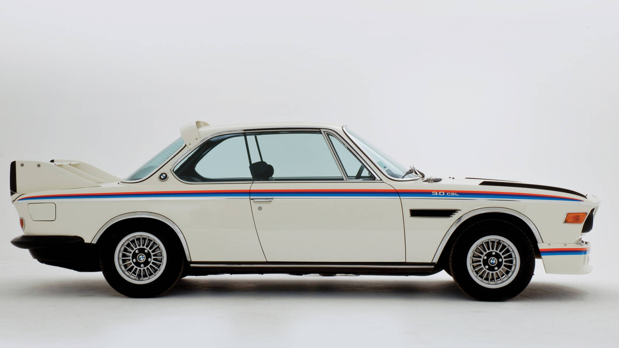classic bmw 桌布 壁紙 — 一架帶有藍色、紅色和黑色條紋的純白色BMW 3.0 CSL賽車，矗立在整潔的攝影棚中。