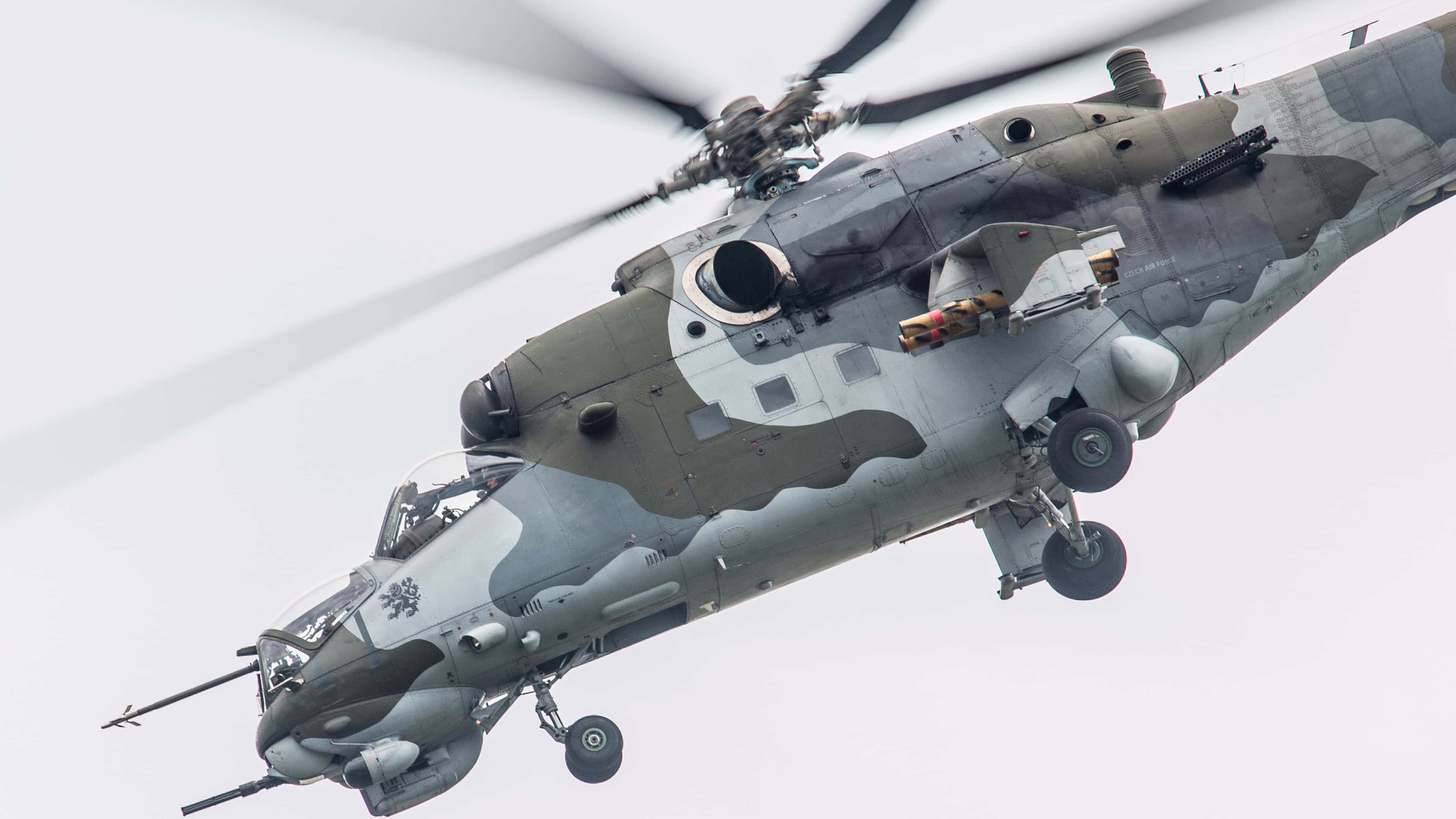 4K Helicopters 桌布 壁紙 — 一架帶有迷彩塗裝的軍用直升機在蒼白的天空下低飛，顯示旋翼葉片在轉動。