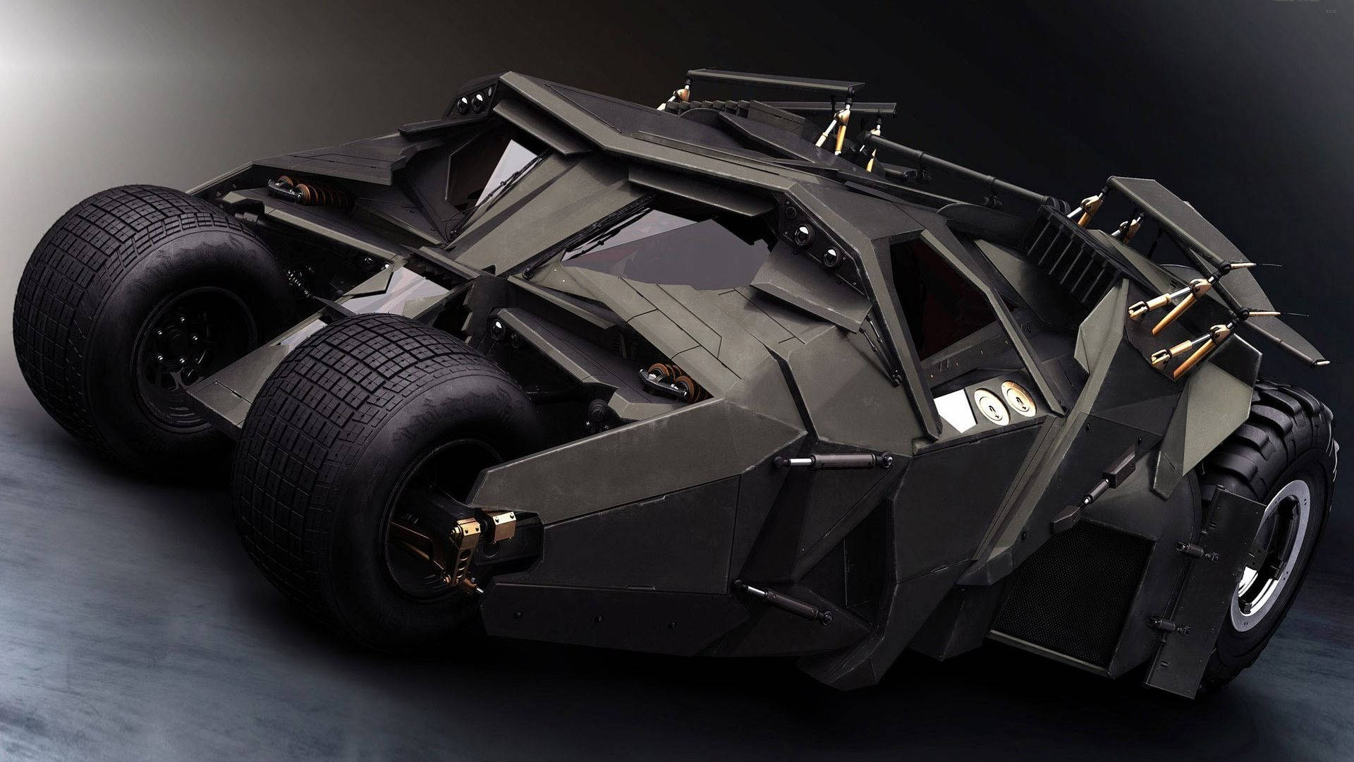Batmobile 桌布 壁紙 — 一架帶有金色裝飾和大輪胎、充滿威脅性的黑色稜角蝙蝠車，在昏暗的攝影棚中擺出戲劇性的姿態。