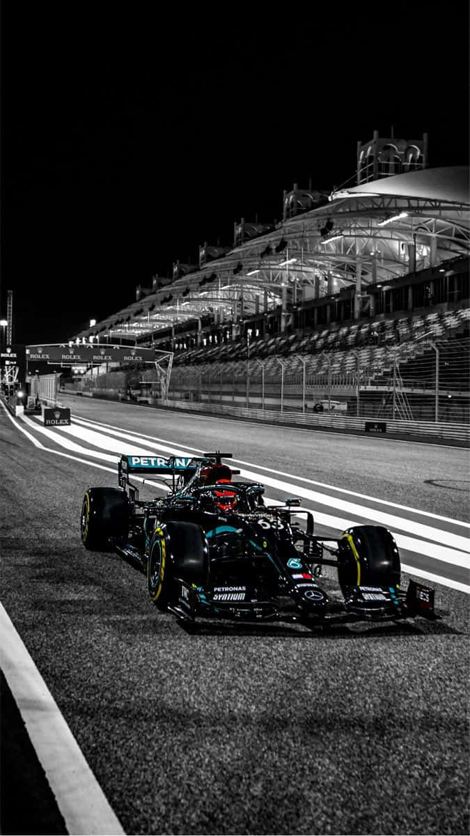 Race Track 桌布 壁紙 — 一架帶有青綠色點綴的流線型一級方程式賽車，在夜間於體育場燈光下的賽道上奔馳。