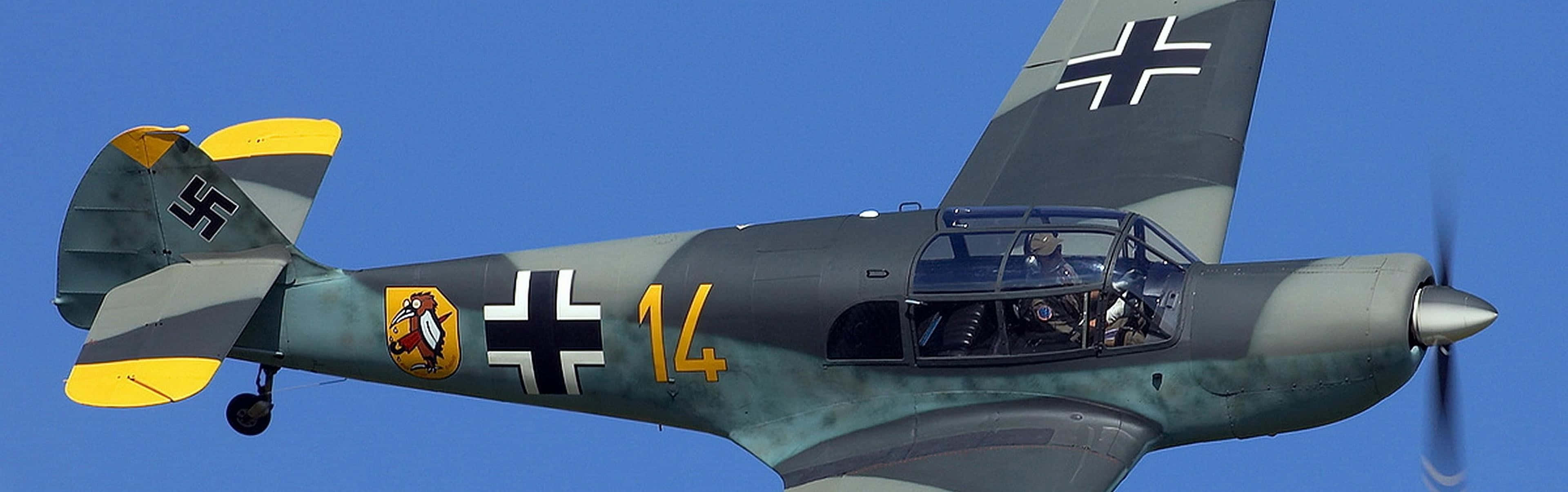 Military Plane 桌布 壁紙 — 一架帶有黑色十字標誌和黃色點綴的復古德國軍用飛機在晴朗的藍天中翱翔。