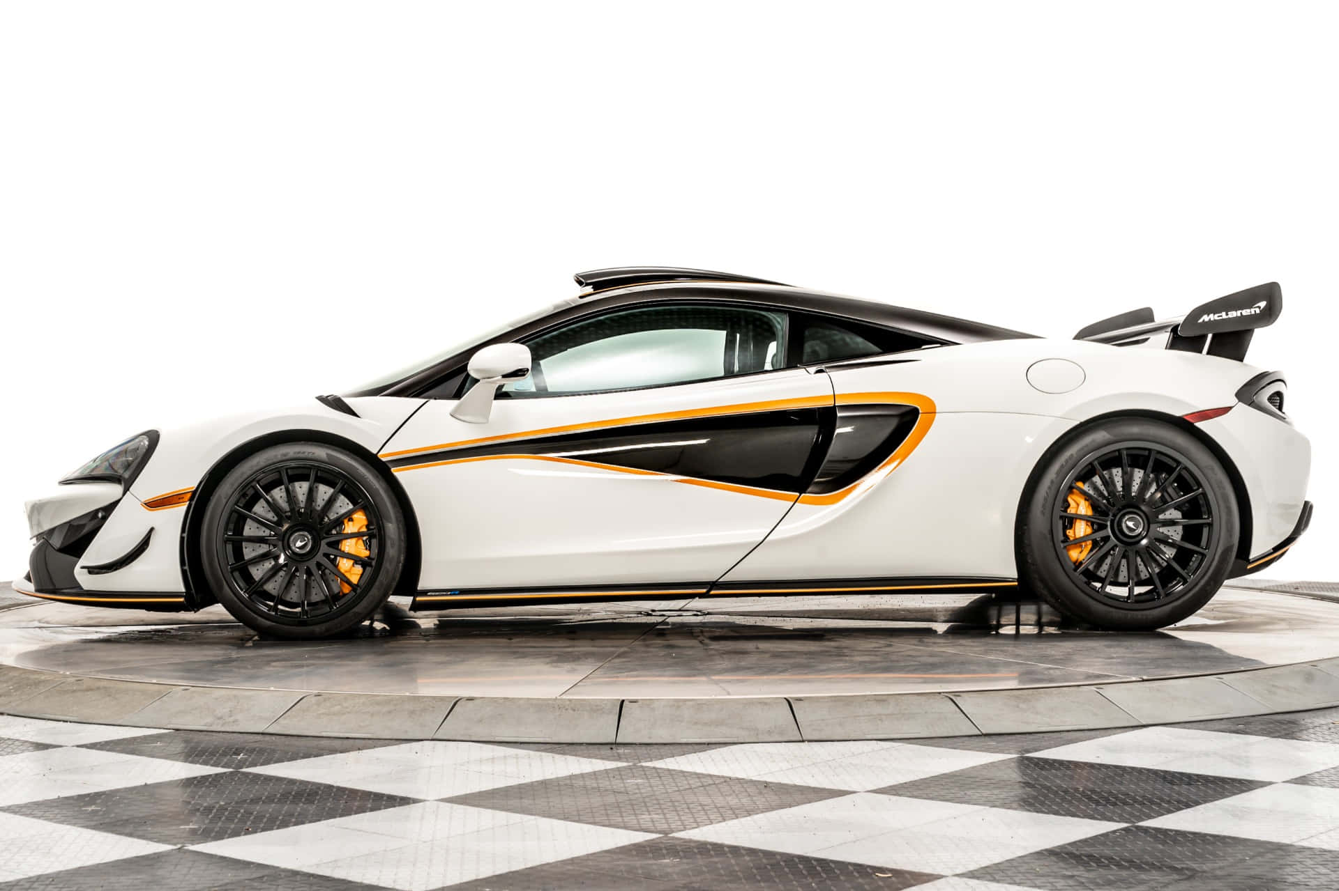 Mclaren 620r 桌布 壁紙 — 一架帶有黑色和橙色點綴的時尚白色McLaren跑車，在棋盤格地板和純白背景上以側面展示。