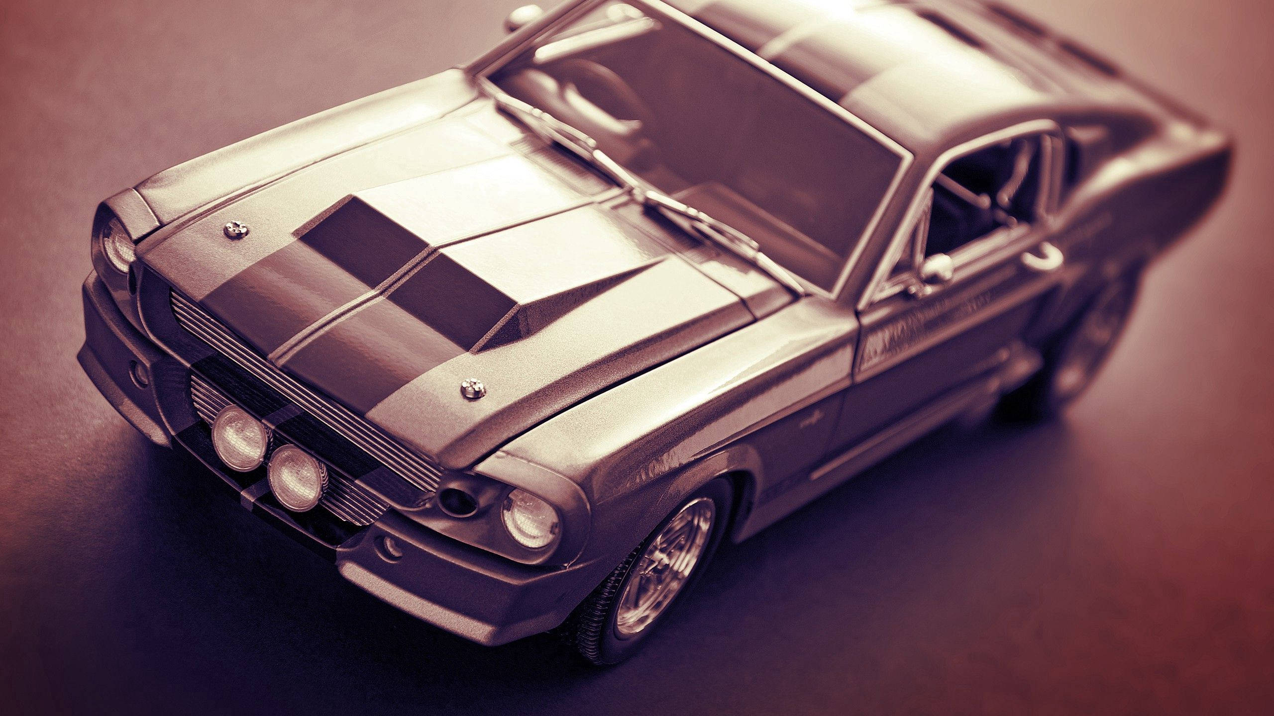 福特 桌布 壁紙 — 一架帶有黑色賽車條紋的復古Shelby Mustang模型車，在溫暖的棕褐色燈光下放置在深色表面上。