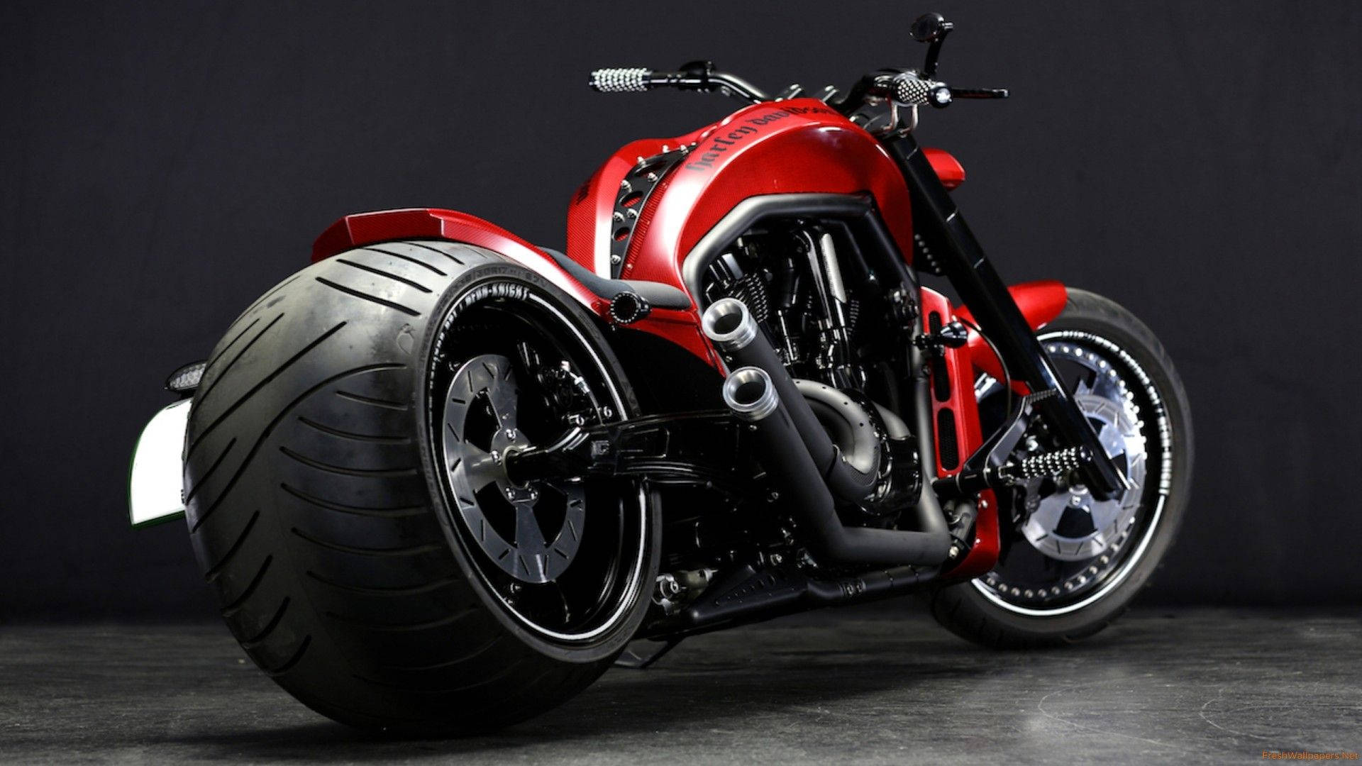 Harley 桌布 壁紙 — 一架引人注目的紅色訂製摩托車，配備巨大前輪胎和裸露引擎，在黑暗的攝影棚背景下展示。