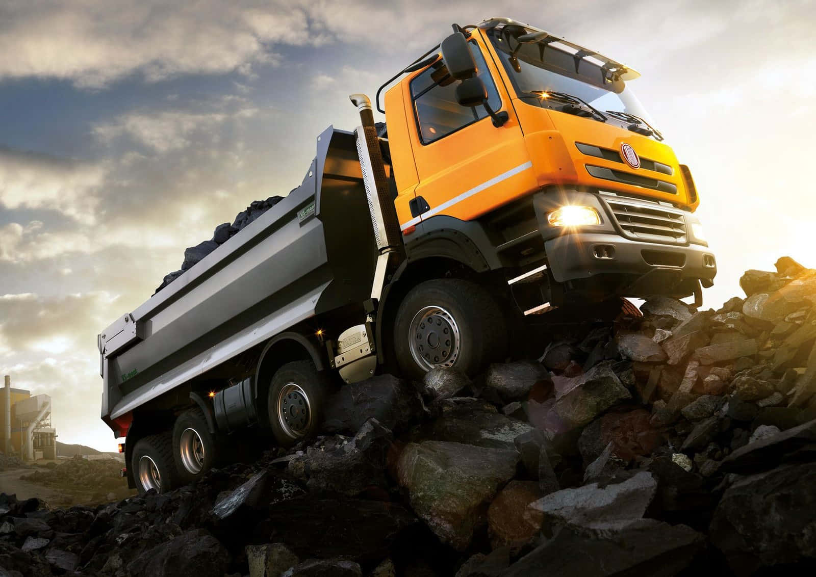 Dump Truck 桌布 壁紙 — 一架強力的橙色自卸車在戲劇性的多雲天空和金色陽光下攀爬岩石山丘。