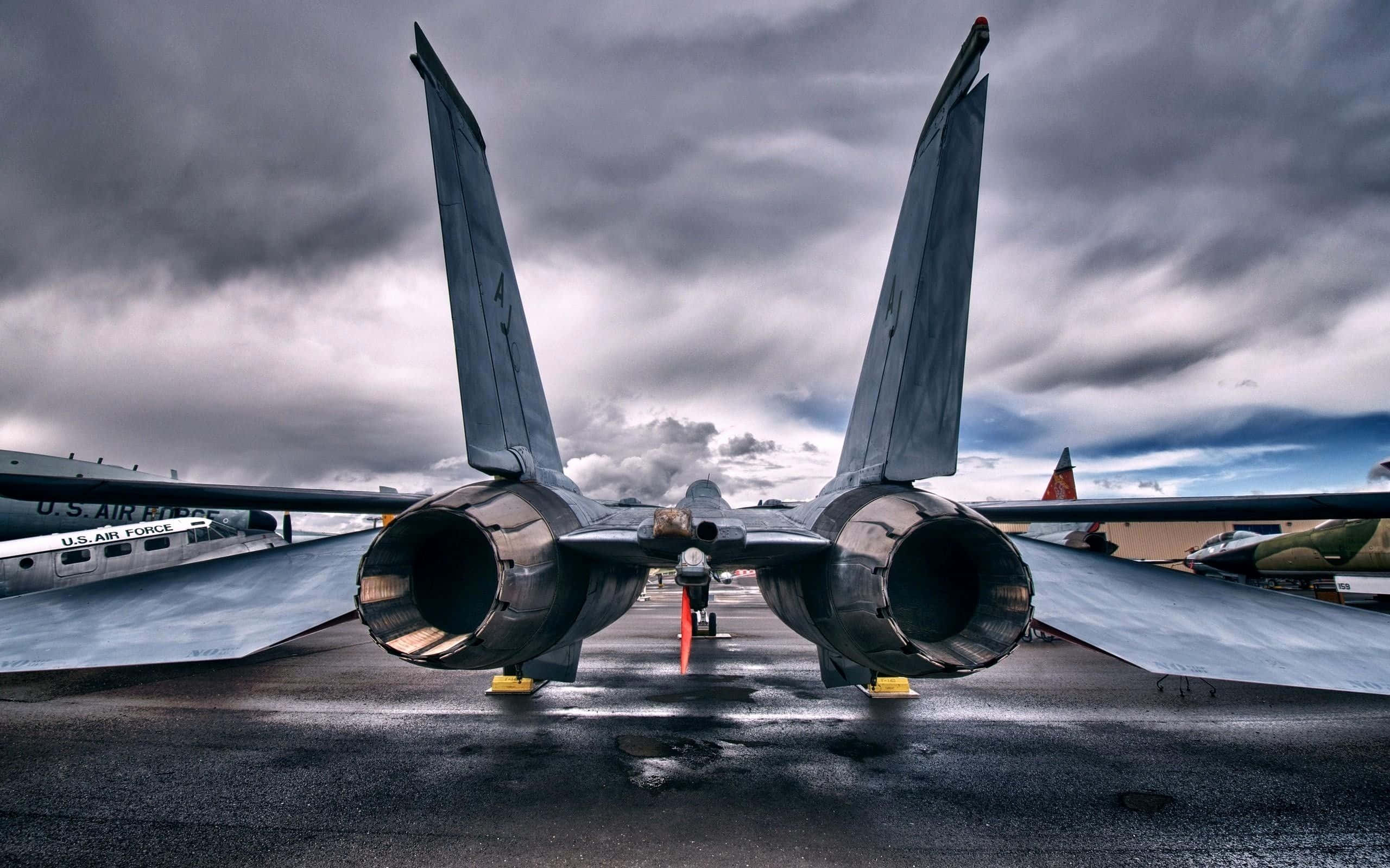 Plane Desktop 桌布 壁紙 — 一架強大的美國空軍戰鬥機在戲劇性的暴風雨天空下佔據濕滑的停機坪，背景有其他飛機。