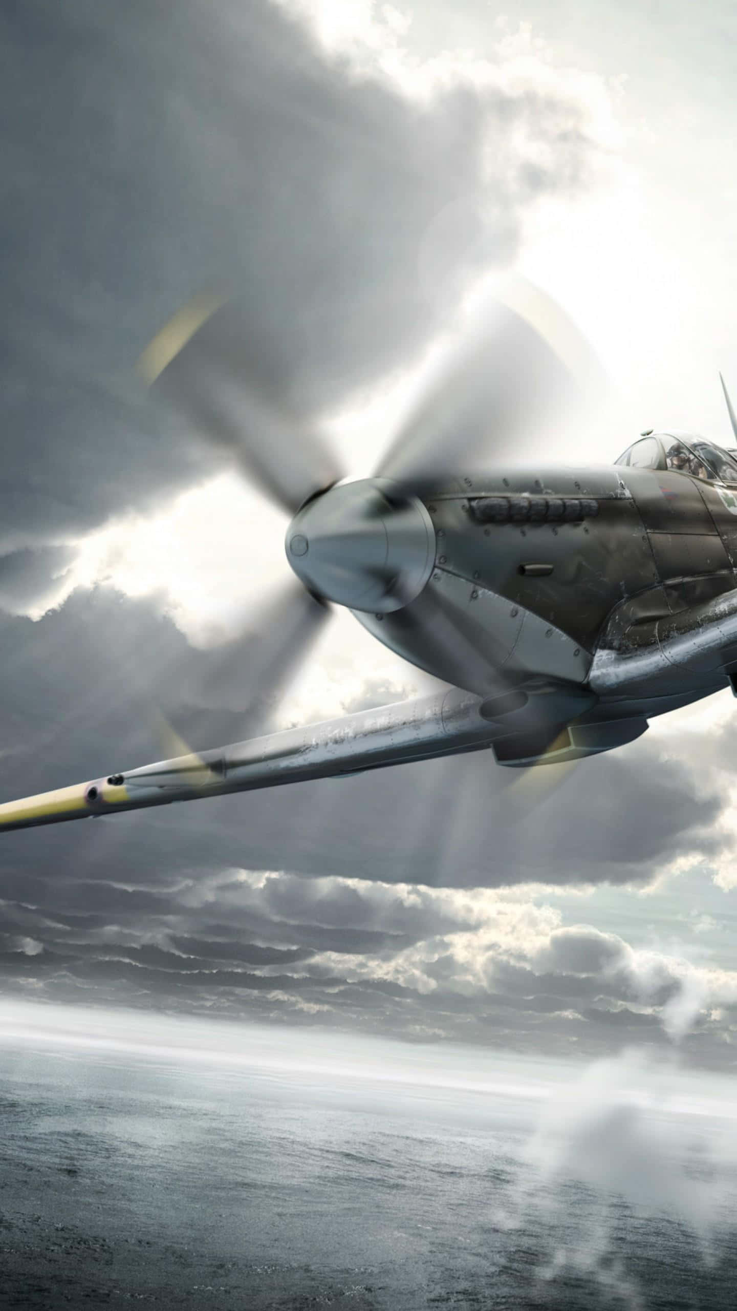 Spitfire 桌布 壁紙 — 一架復古戰鬥機在波濤洶湧的海面上低空飛翔，戲劇性的陽光穿透烏雲。