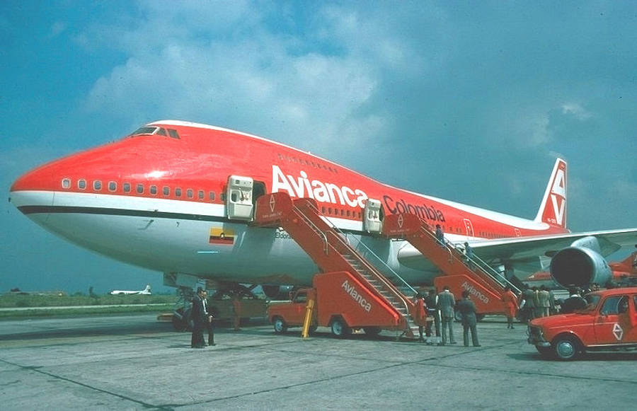 Plane 桌布 壁紙 — 一架復古紅白色Avianca Colombia波音747停泊在停機坪上，乘客正在部分多雲的天空下通過移動樓梯登機。