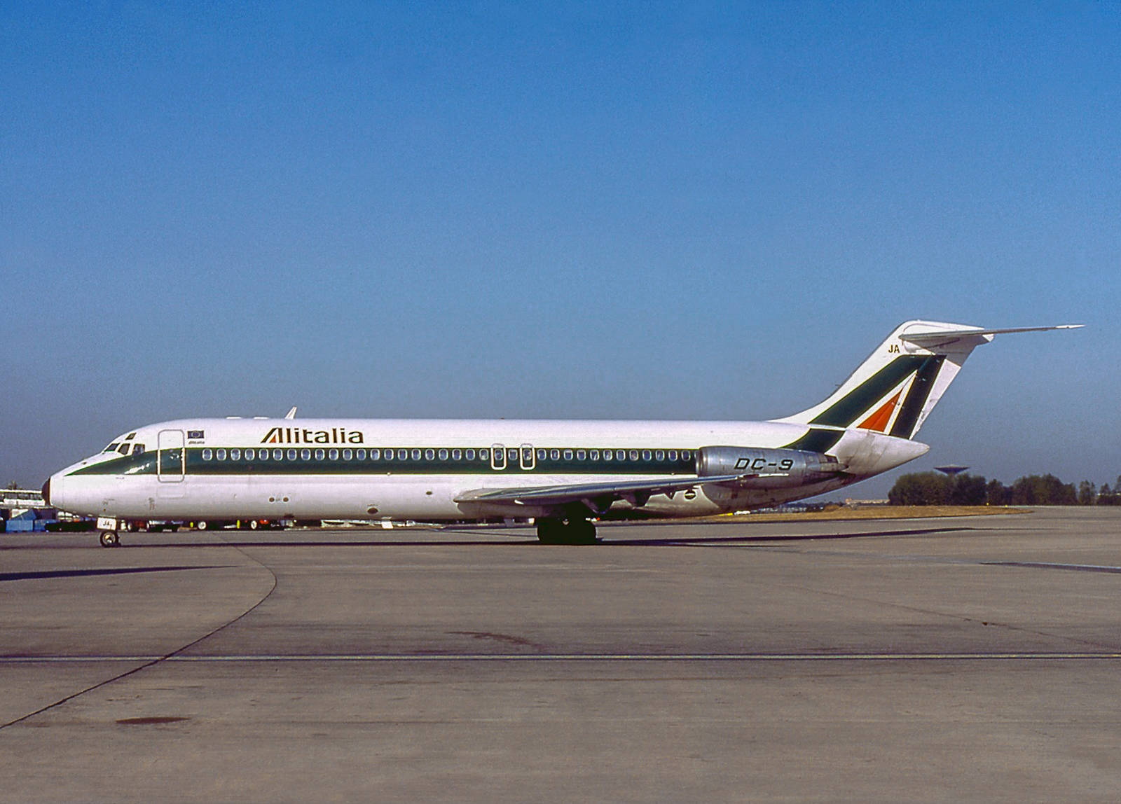 飛機 桌布 壁紙 — 一架復古義大利航空 DC-9 飛機在晴朗藍天下停泊在陽光明媚的機場停機坪上。