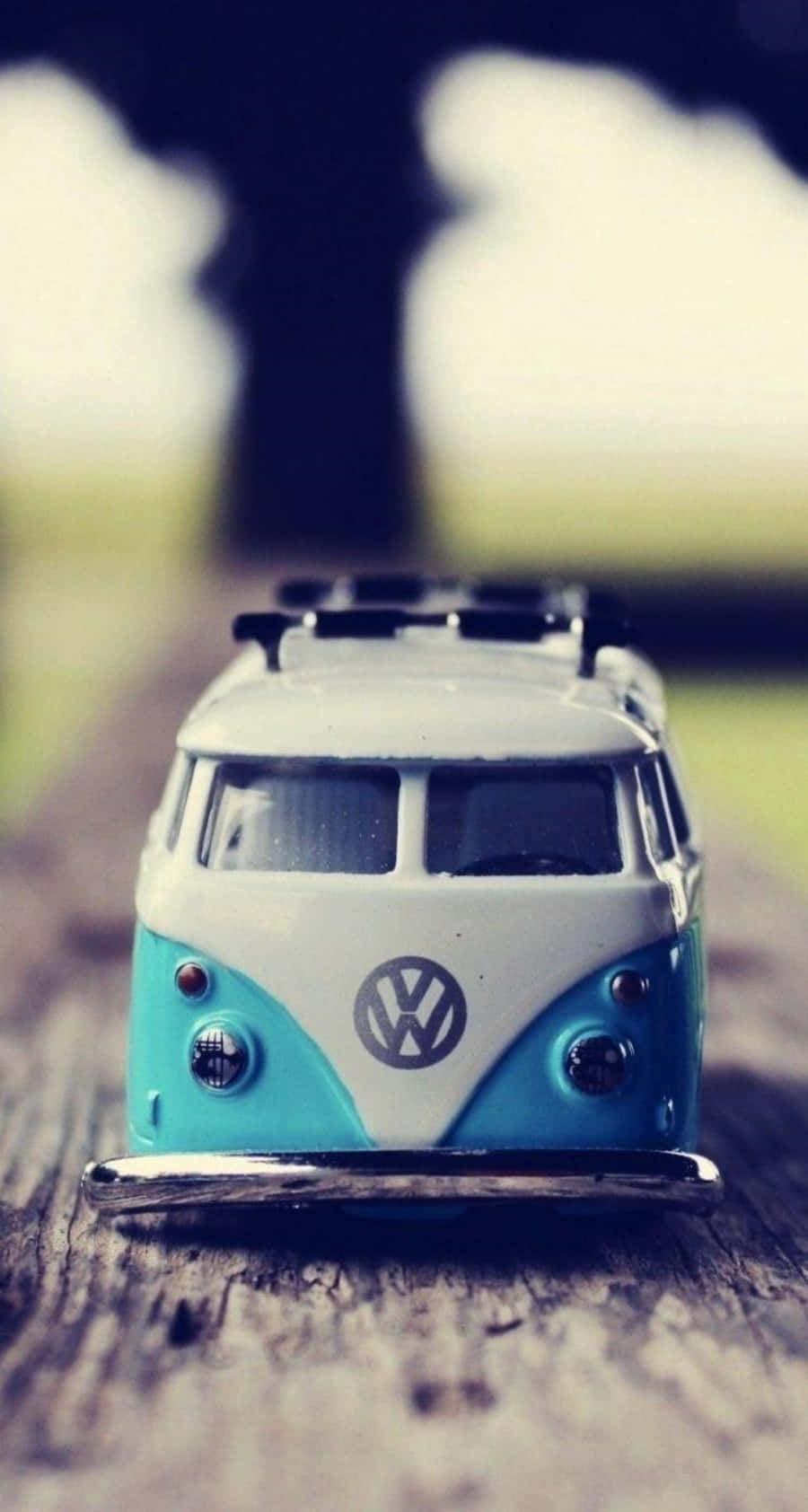 Van 桌布 壁紙 — 一架復古藍綠色和白色的福斯偉根廂型車玩具放在風化木上，背景模糊的戶外景色。