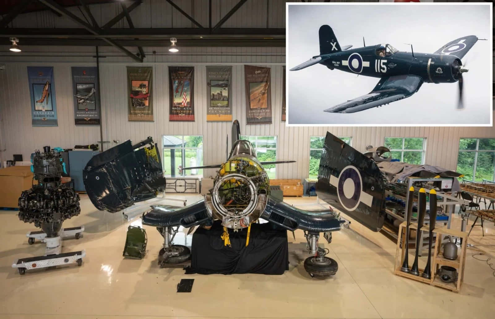 海盜船 桌布 壁紙 — 一架復古軍用飛機在機庫中展出，機身打開露出引擎部件和拆卸的機翼，周圍環繞著航空紀念品。