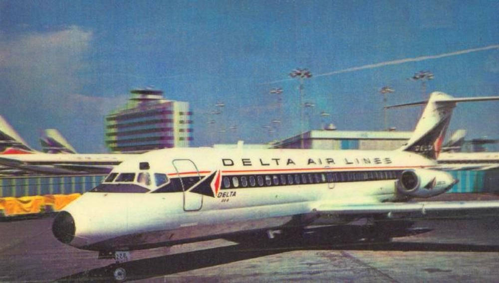 飛機 桌布 壁紙 — 一架復古達美航空噴射客機停泊在機場停機坪上，背景是晴朗的藍天和現代建築。