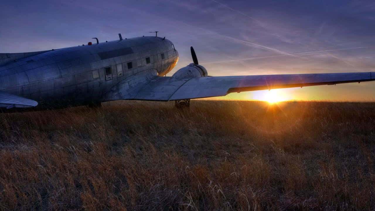 飛機 桌布 壁紙 — 一架復古金屬飛機停在高高的金色草地上，夕陽在它身後落下，散發出溫暖的光芒。