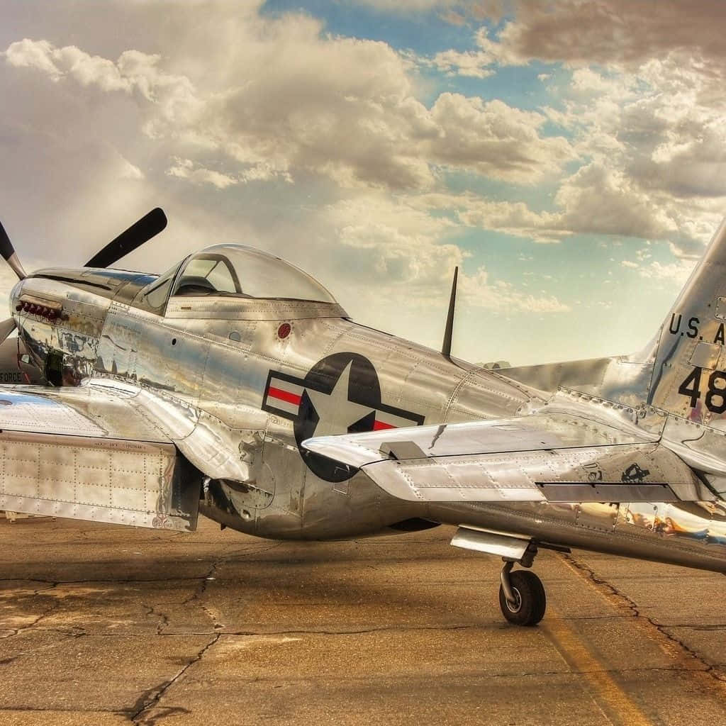 Air Force 桌布 壁紙 — 一架復古銀色P-51野馬戰鬥機停在裂開的停機坪上，背景是戲劇性的多雲天空。