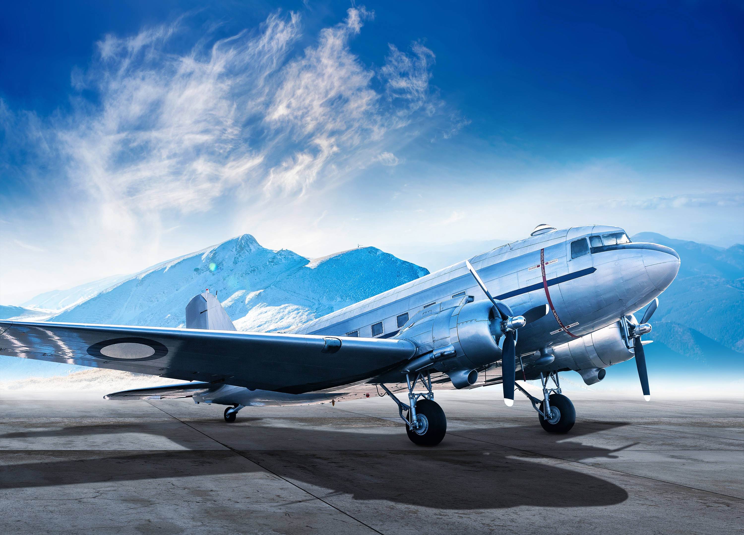 HD Plane 桌布 壁紙 — 一架復古銀色螺旋槳飛機停在停機坪上，背景是白雪覆蓋的山脈和明亮的藍天。