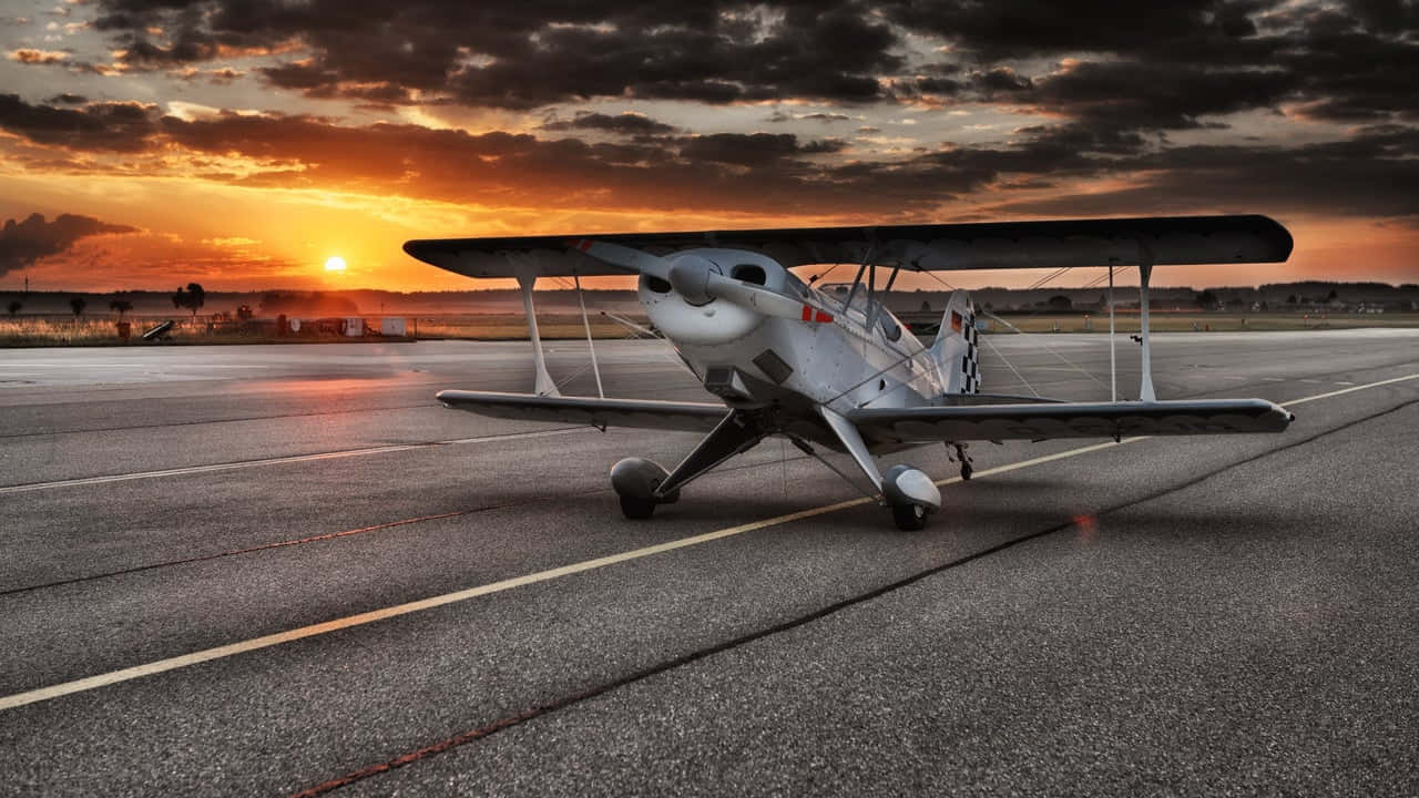 Aviation 桌布 壁紙 — 一架復古雙翼飛機停在跑道上，夕陽在戲劇性的橙色和灰色雲層後落下。