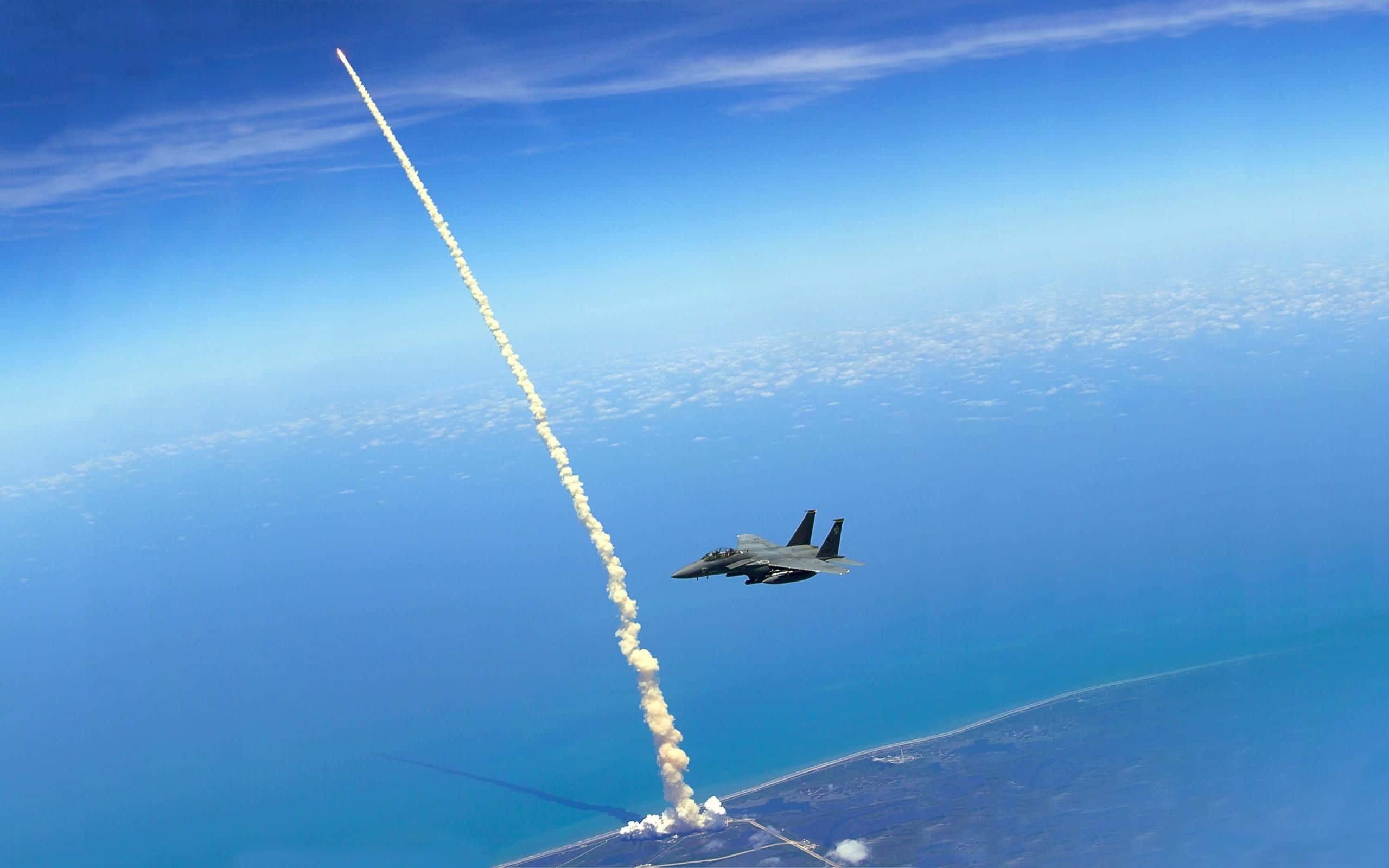 space shuttle 桌布 壁紙 — 一架戰鬥機在地球彎曲的地平線上空翱翔，在清澈的藍天上留下煙跡。