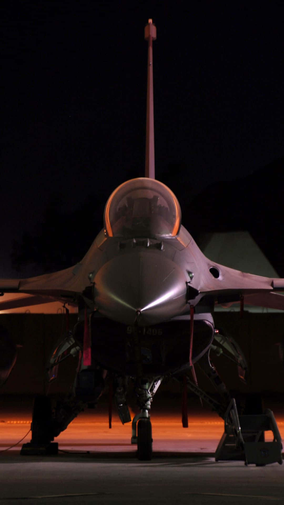 Android Jumbo Jets 桌布 壁紙 — 一架戰鬥機在夜間停放在停機坪上，在黑暗的天空下被溫暖的橙色地面燈光照亮。