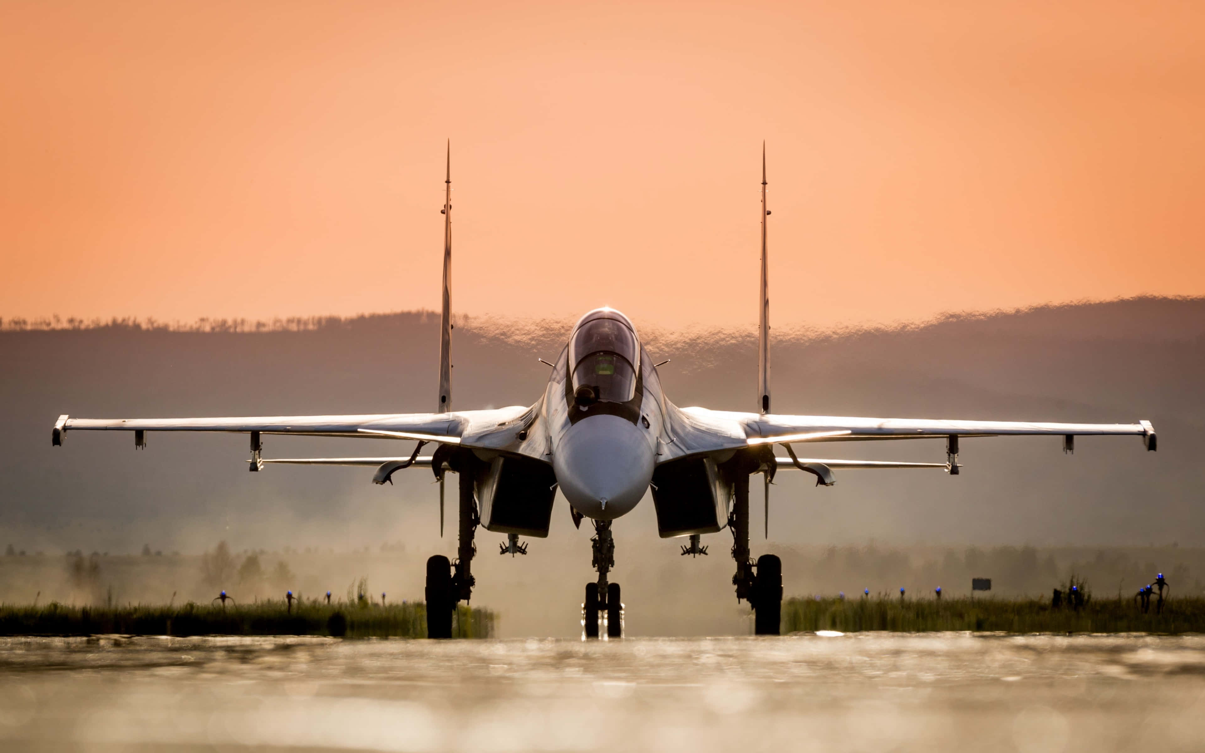 4K Military 桌布 壁紙 — 一架戰鬥機在日出時面向潮濕跑道，橙色天空和遠山。
