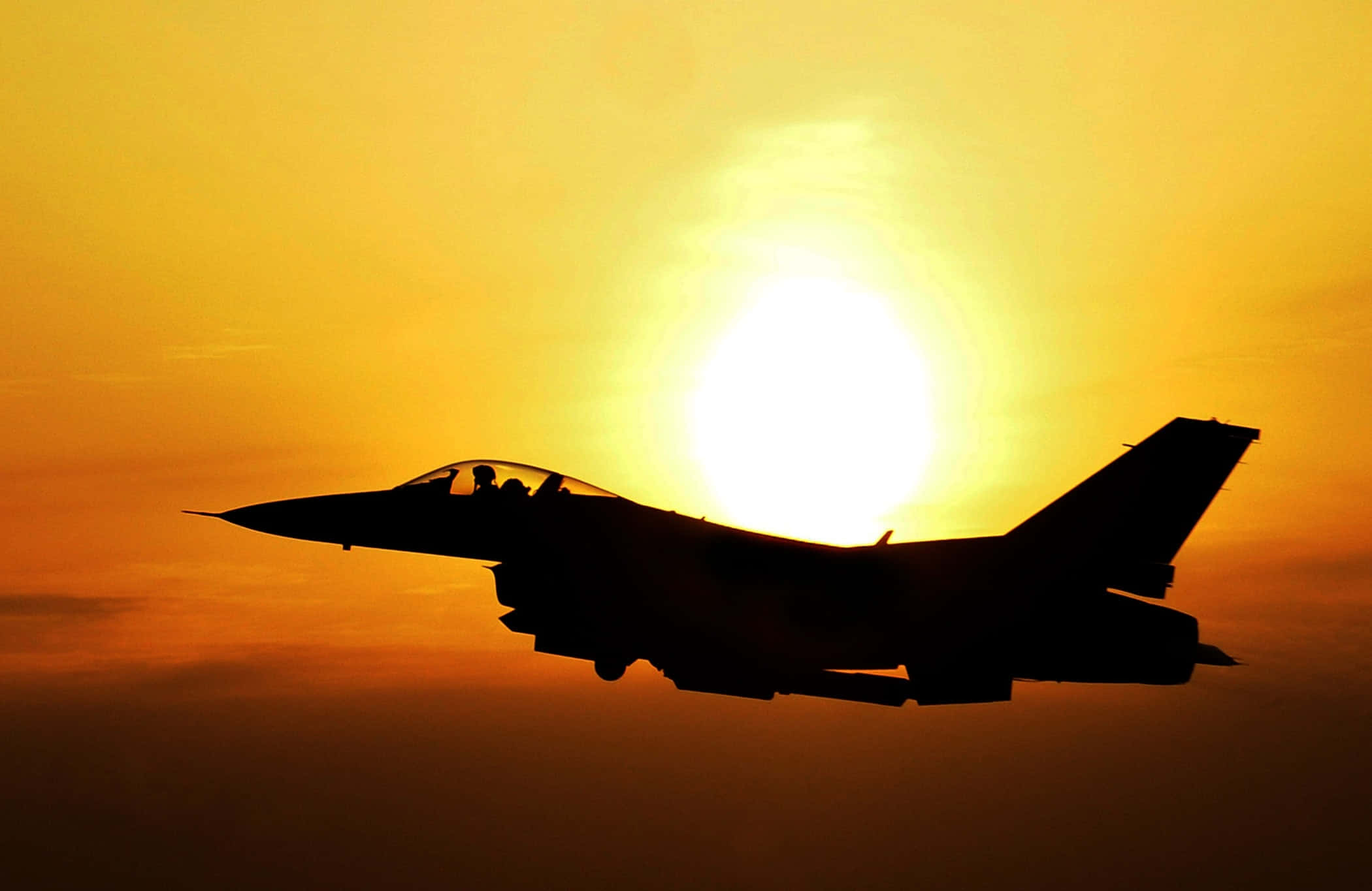Fighter Jet 桌布 壁紙 — 一架戰鬥機在溫暖的橙色和黃色色調的發光日落天空背景下形成剪影。