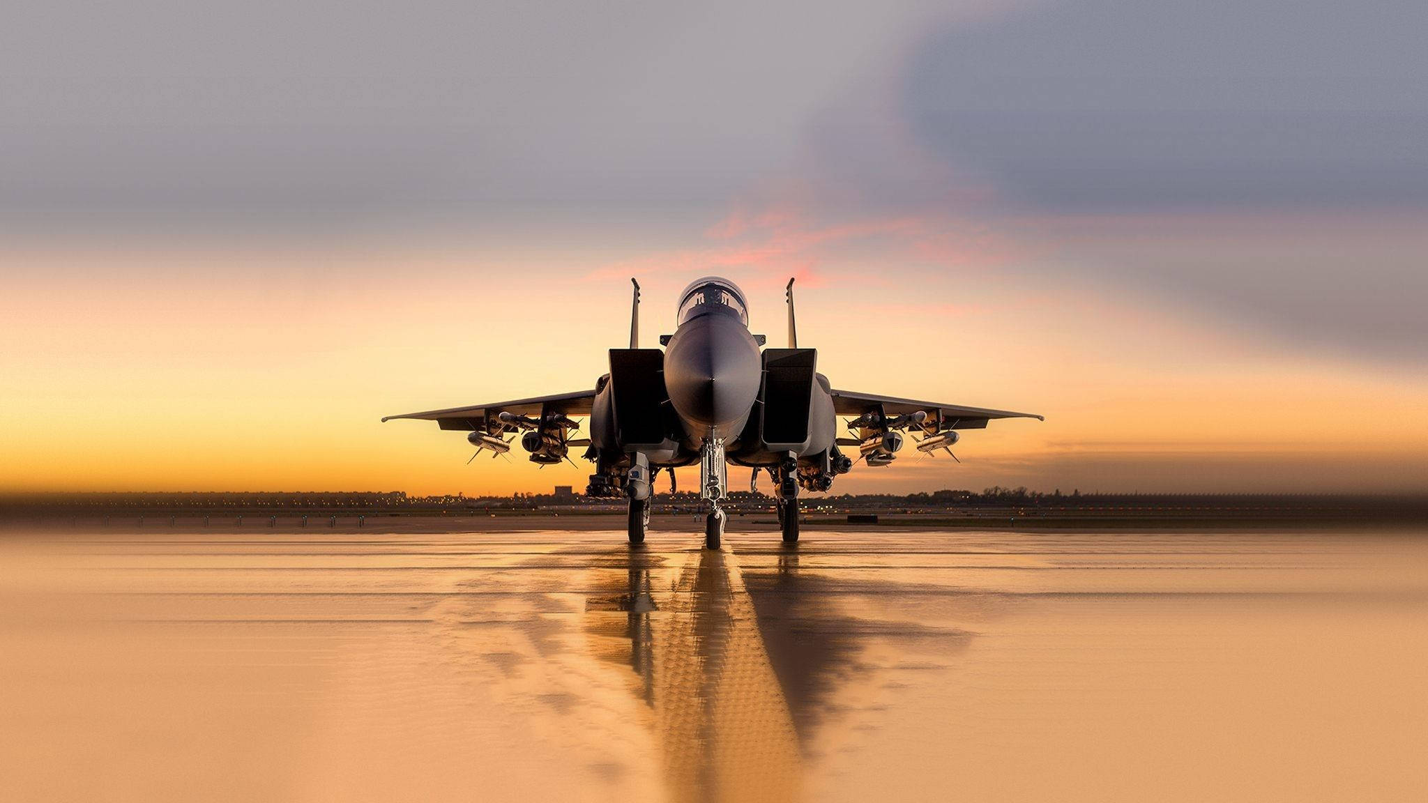 Military Jets 桌布 壁紙 — 一架戰鬥機在濕滑的停機坪上蓄勢待發，金色的夕陽光線映照在地面和天空中。