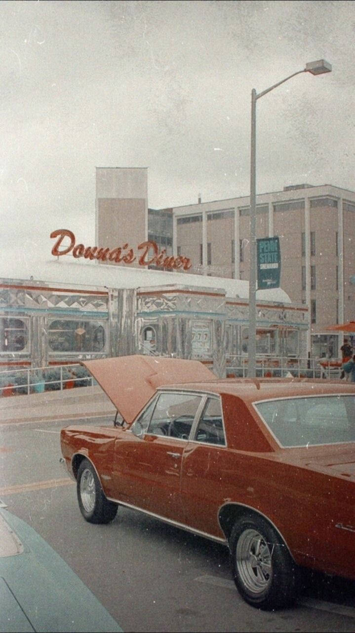 美學 桌布 壁紙 — 一架打開引擎蓋的復古紅色汽車停放在Donna's Diner前面，天空多雲。