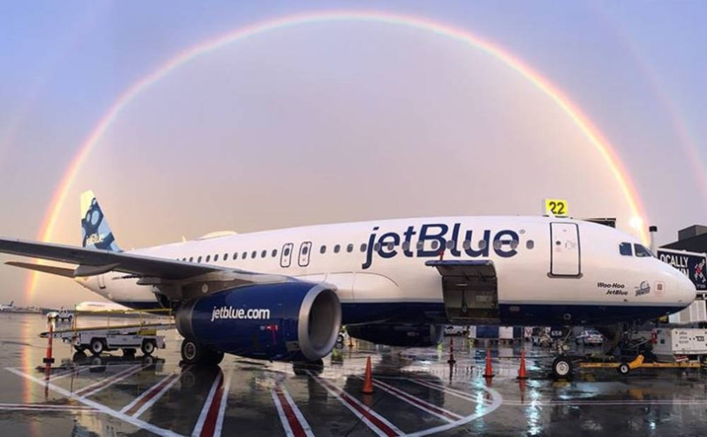 飛機 桌布 壁紙 — 一架捷藍航空飛機停在濕滑的停機坪上，暮色中一道鮮豔的彩虹橫跨天空。