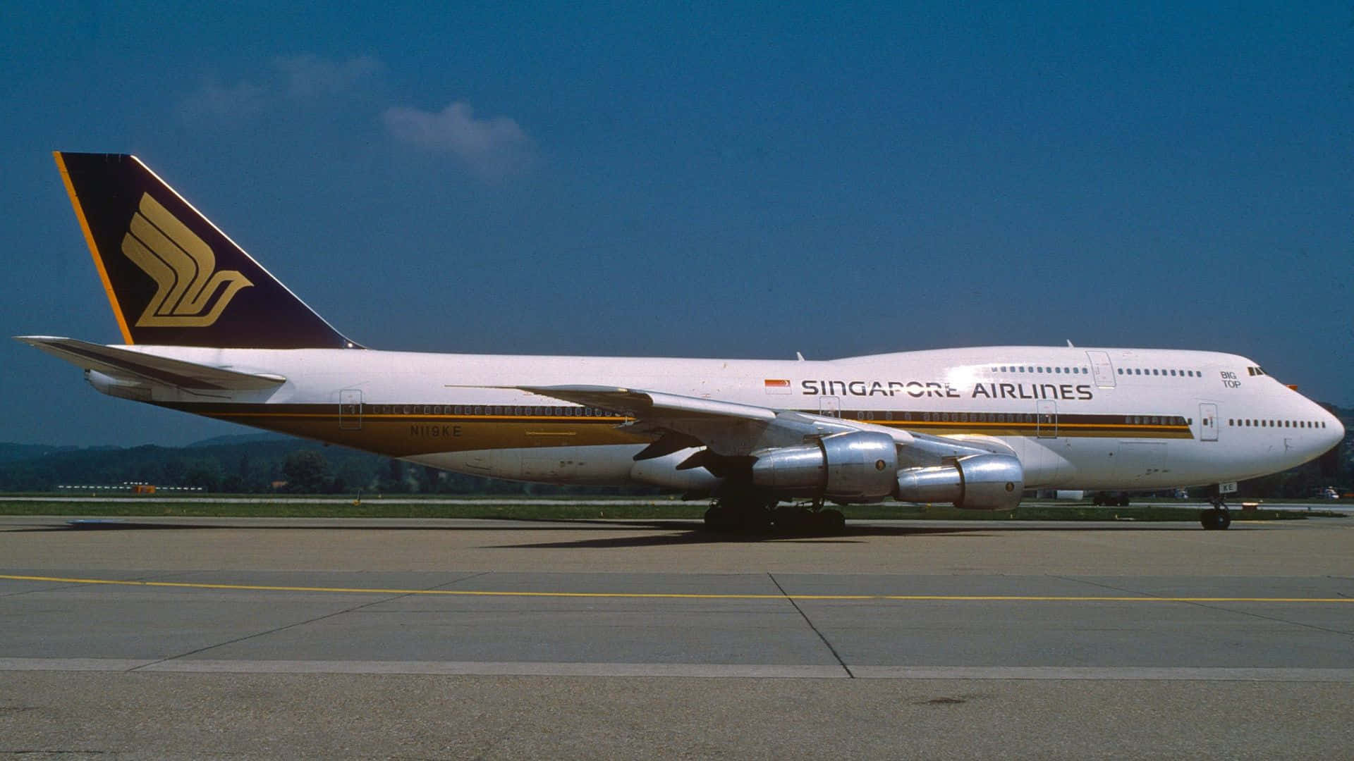 1920x1080 Jumbo Jets 桌布 壁紙 — 一架新加坡航空的波音747停放在陽光普照的停機坪上，天空清澈湛藍，遠方有山丘。