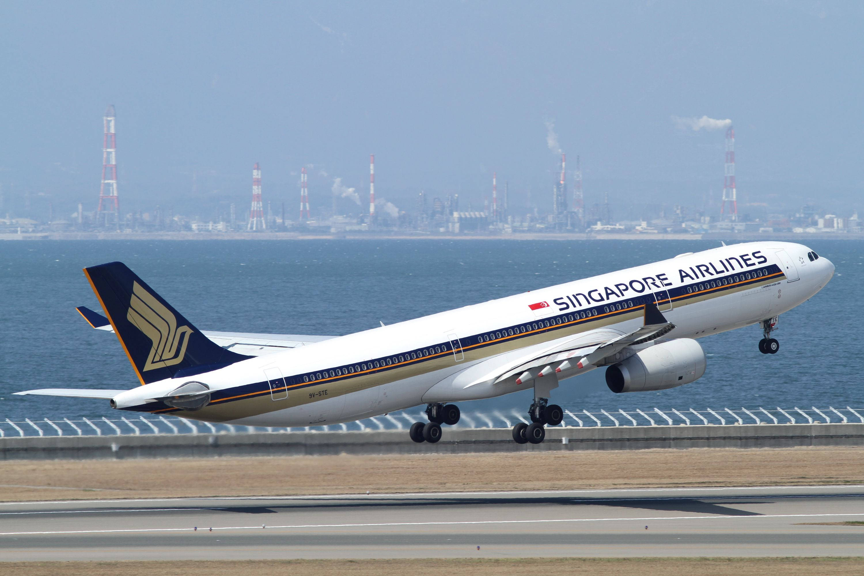 Singapore 桌布 壁紙 — 一架新加坡航空的空中巴士A330正在跑道上降落，背景是沿海工業天際線和藍色大海。