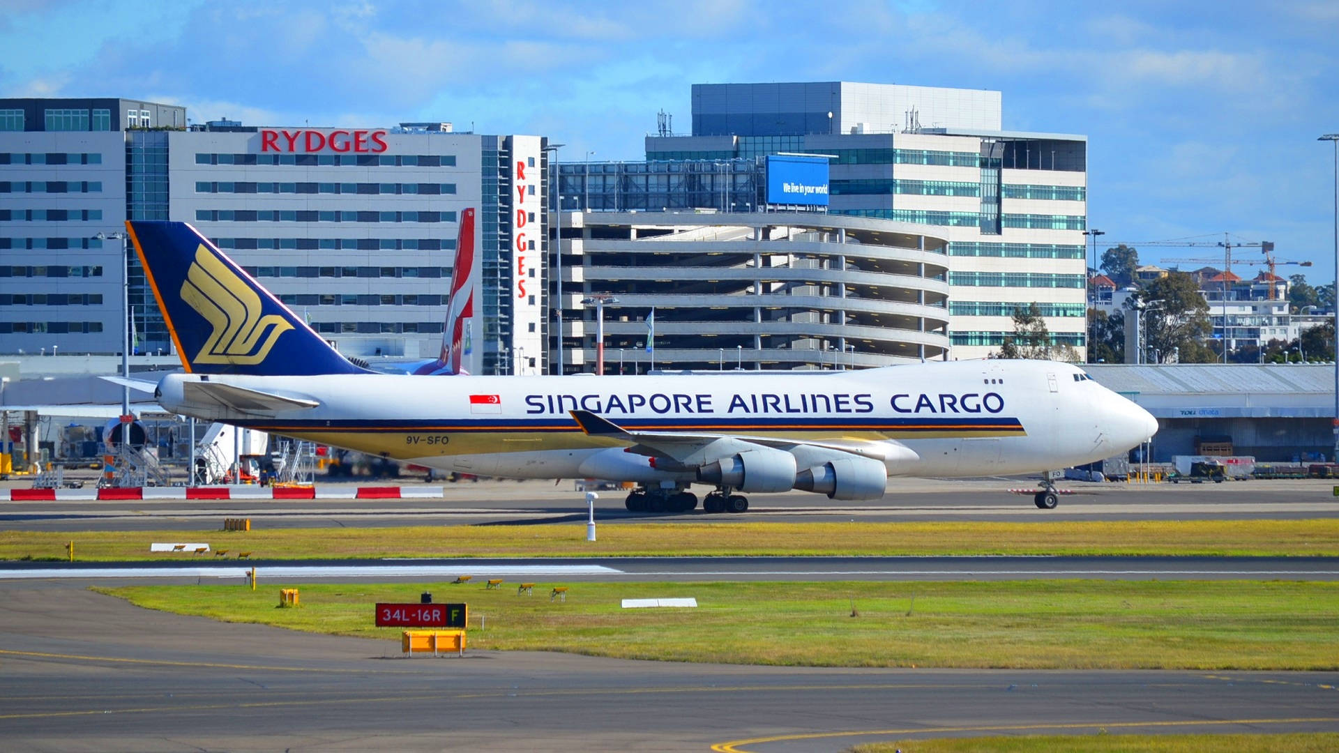 機場 桌布 壁紙 — 一架新加坡航空貨運波音747在陽光明媚的機場停機坪上滑行，背景有現代建築和清澈的藍天。