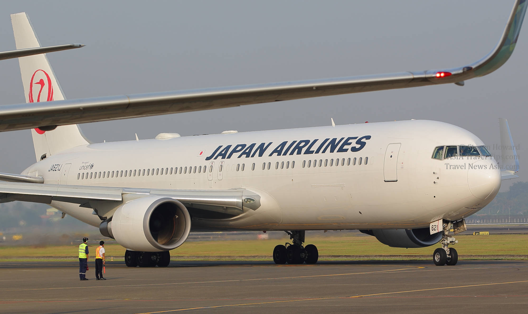 日本 桌布 壁紙 — 一架日本航空客機在跑道上滑行，地勤人員在朦朧的日光下站在附近。