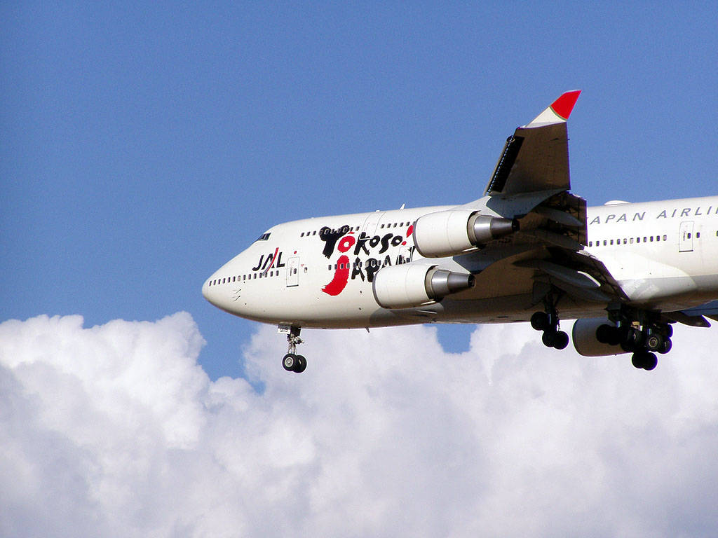 飛機 桌布 壁紙 — 一架日本航空波音747帶有「Yokoso Japan」塗裝，在晴朗藍天中穿過蓬鬆白雲下降。
