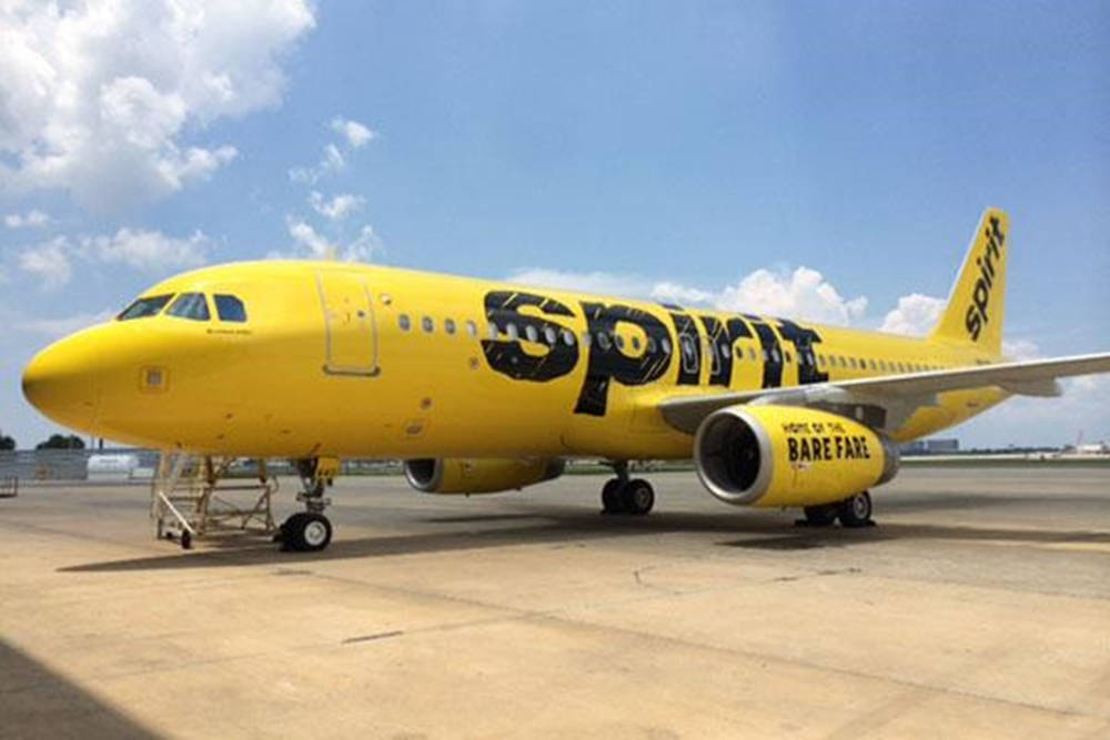 飛機 桌布 壁紙 — 一架明亮的黃色Spirit Airlines噴射機，引擎上寫有「BAREFARE」，停在部分多雲的藍天下停機坪上。