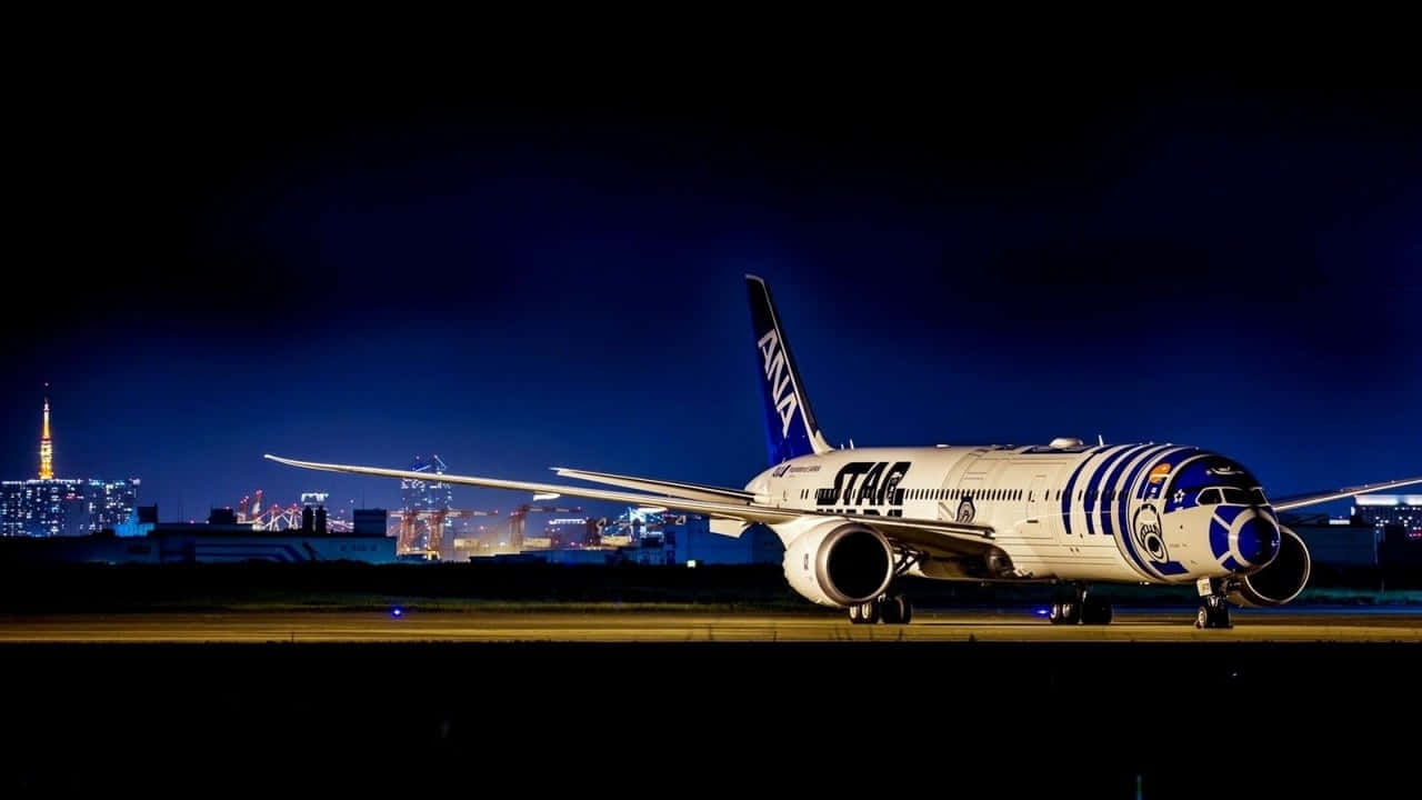 飛機 桌布 壁紙 — 一架星戰主題ANA飛機帶有R2-D2塗裝，夜晚停在跑道上，背後東京天際線燈光閃爍。