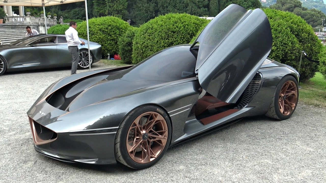 Genesis Essentia 桌布 壁紙 — 一架時尚未來感跑車，配備鷗翼車門和銅色輪圈，停泊在碎石路上，旁邊是修剪整齊的樹籬。